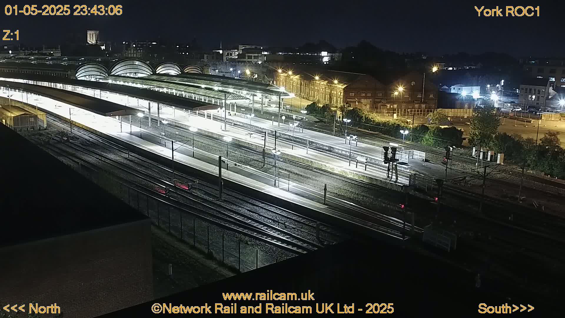 A nighttime aerial view of a brightly lit train station with numerous tracks and platforms.