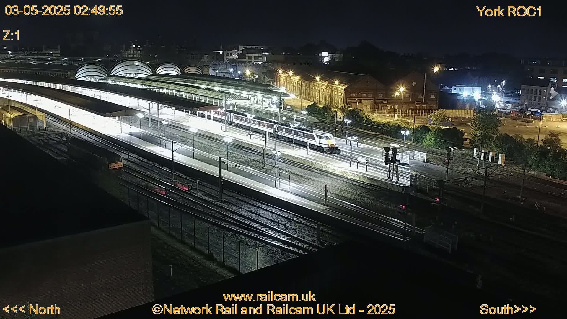 A brightly lit train station at night with a passenger train on the tracks.