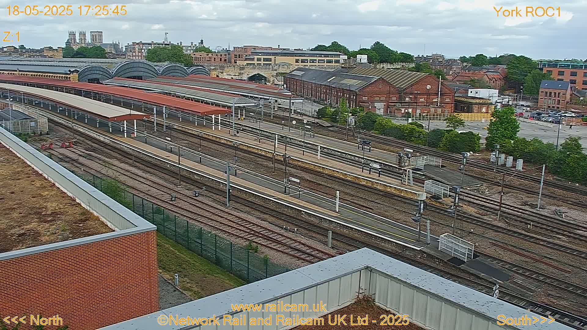 A high-angle, daytime view of a railway station with numerous tracks and platforms under a partly cloudy sky.