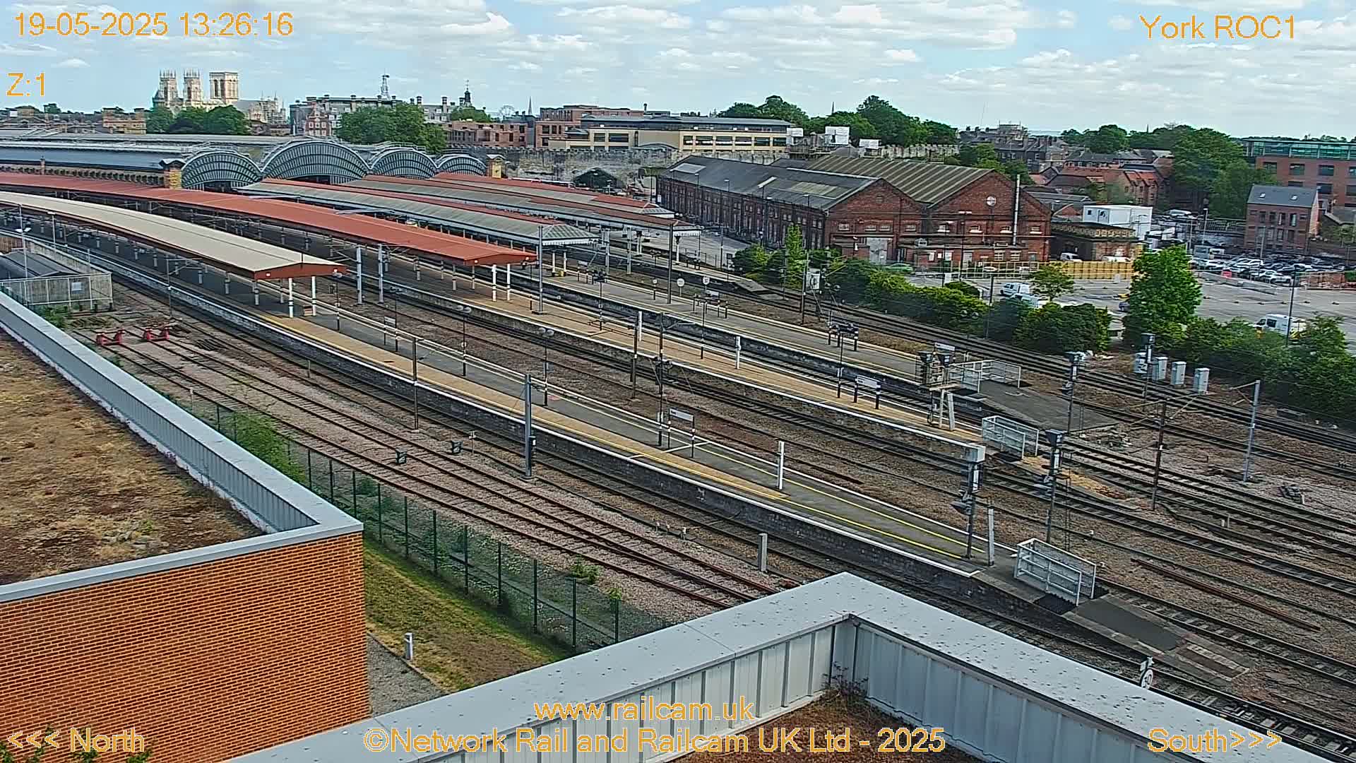A high-angle view of a train station with numerous tracks and platforms under a partly cloudy sky.