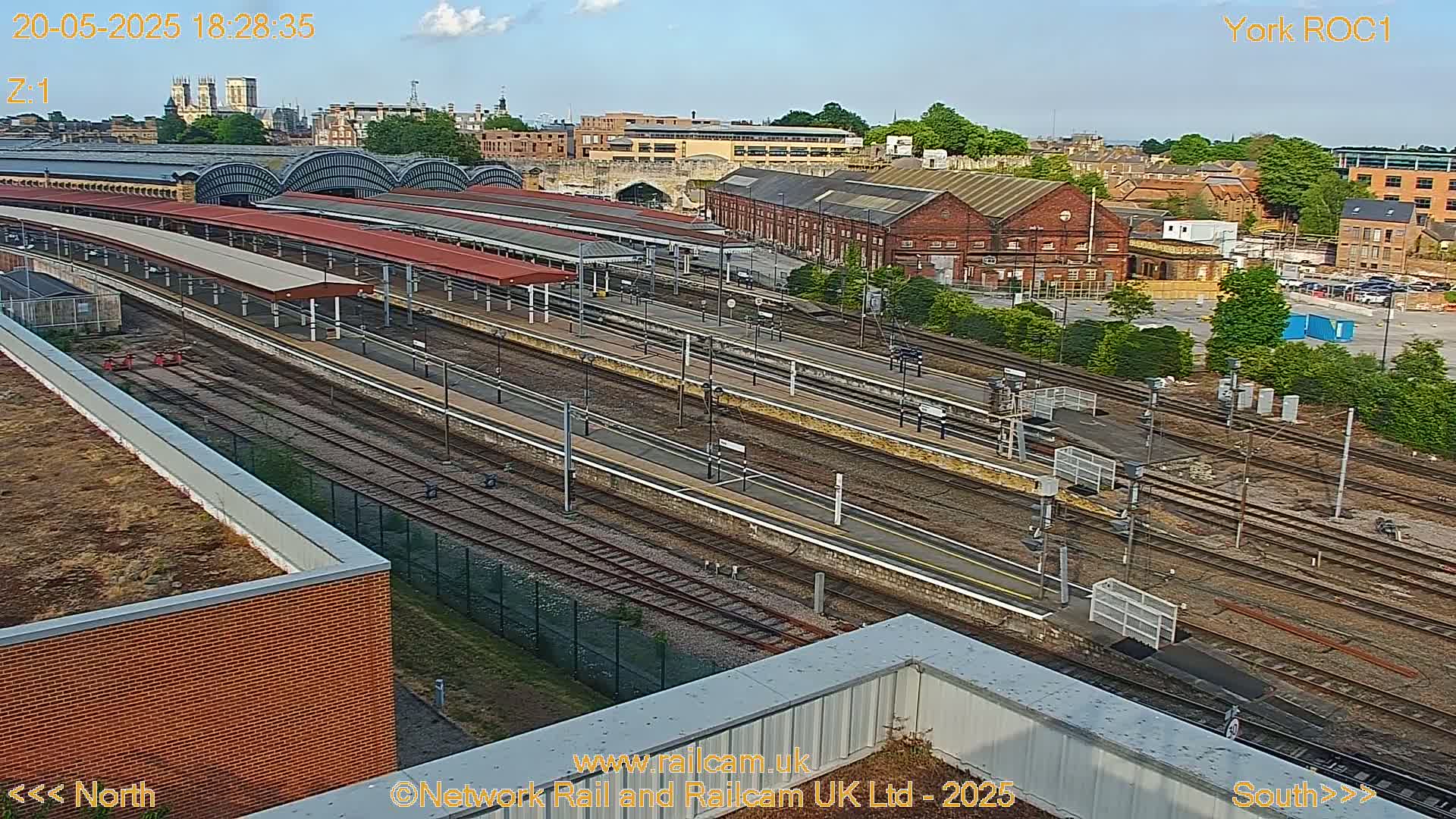 A high-angle view of a train station with many tracks and platforms under a partly cloudy sky.
