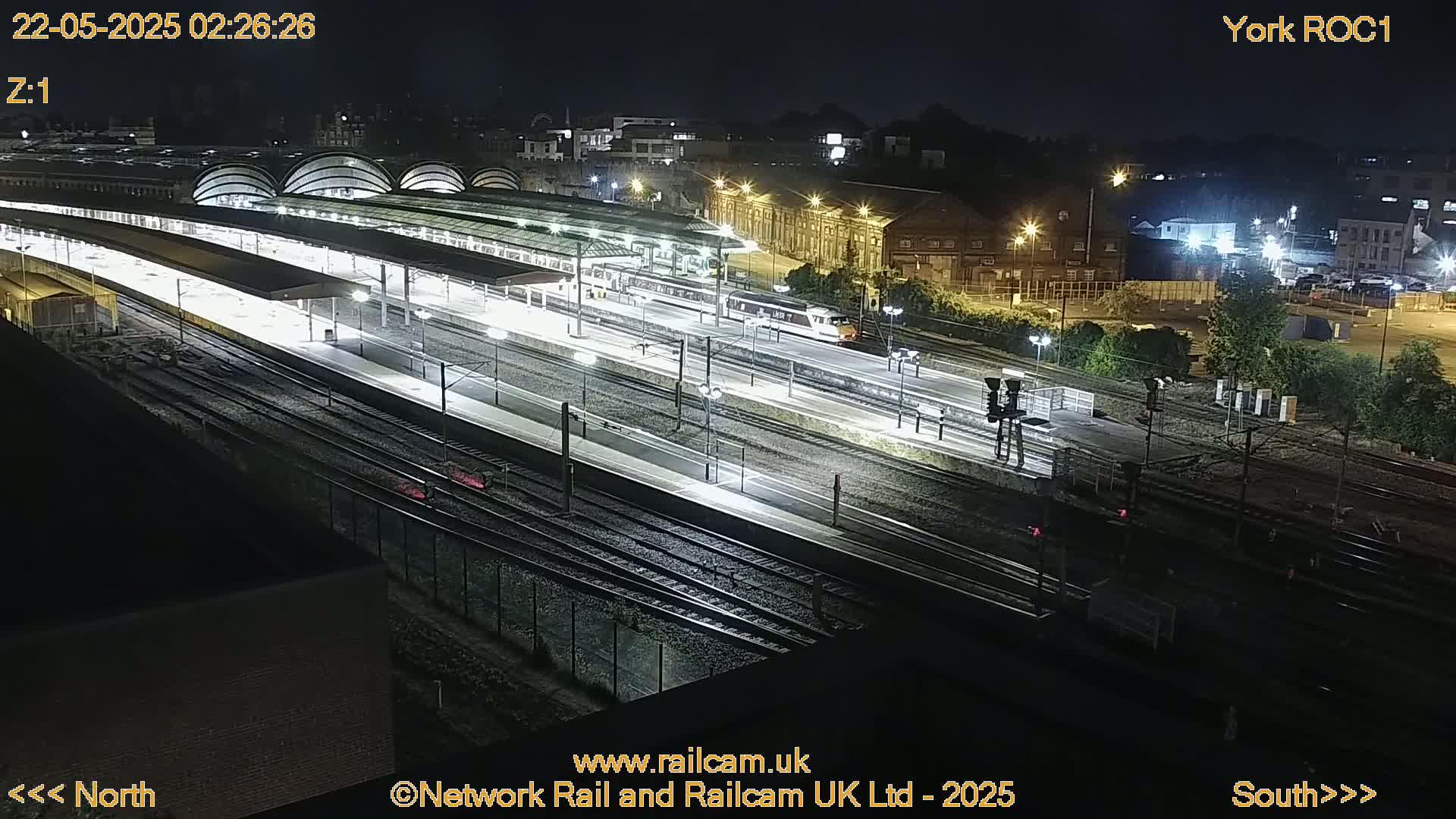 A brightly lit train station at night with a train on the tracks.