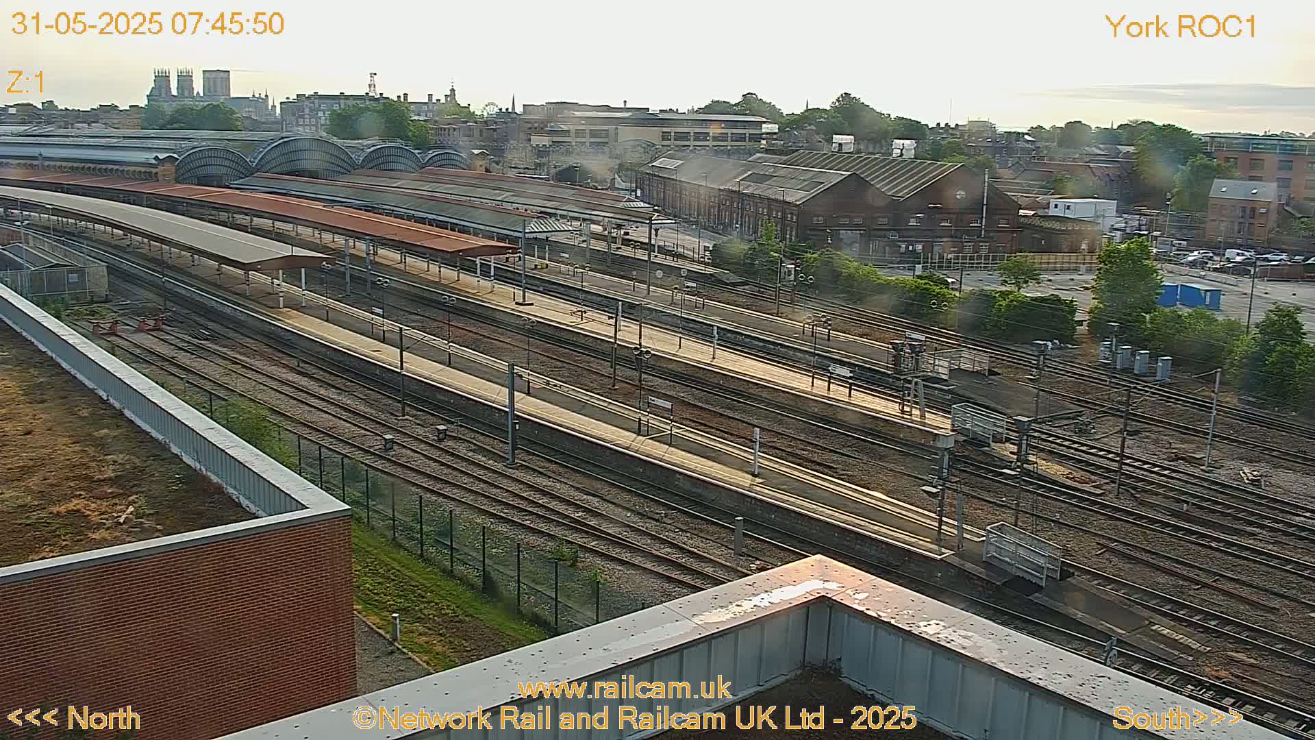 A high-angle view of a train station with numerous tracks and platforms, under a partly cloudy sky.