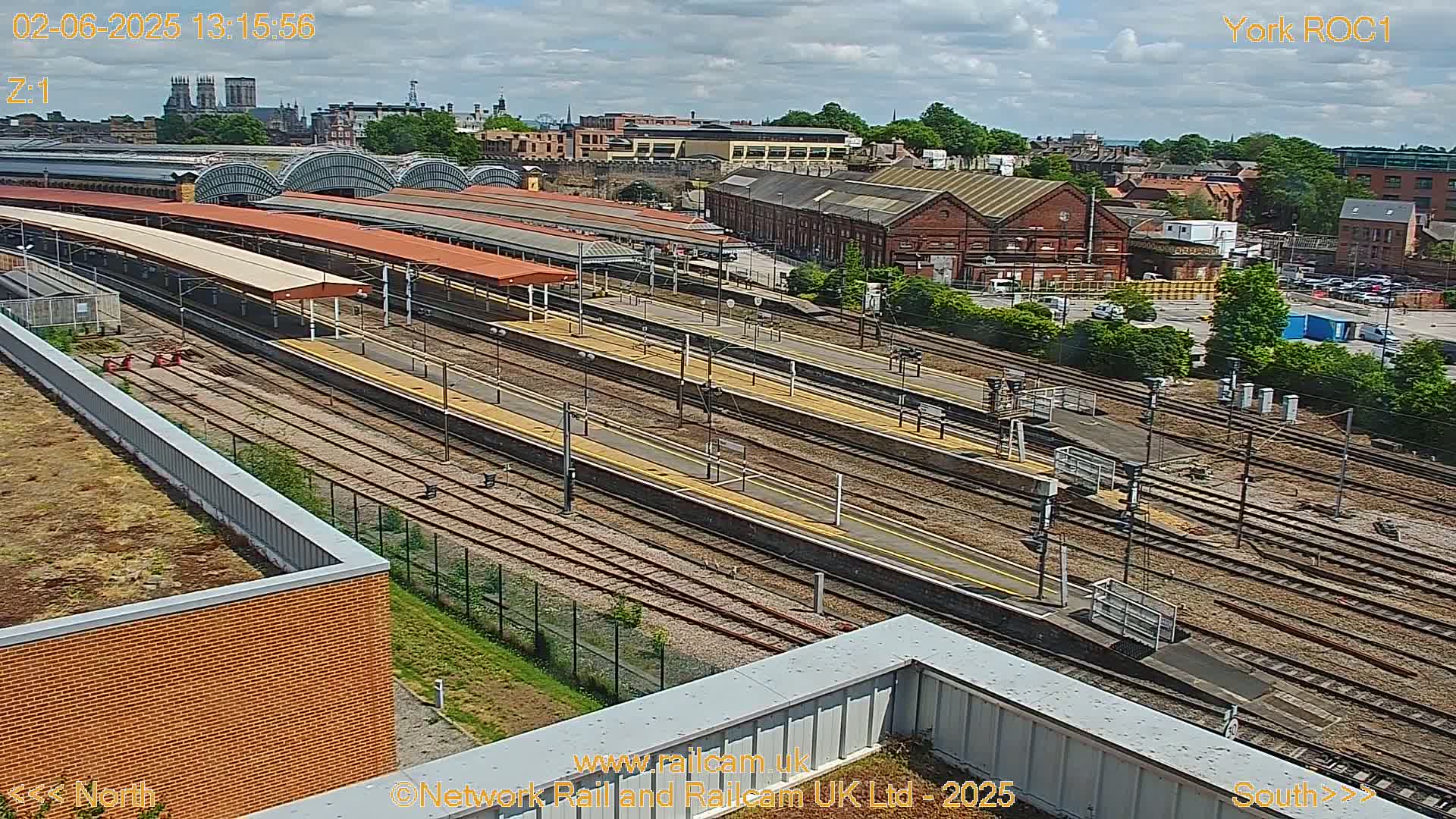 A high-angle view of a train station with numerous tracks and platforms under a partly cloudy sky.