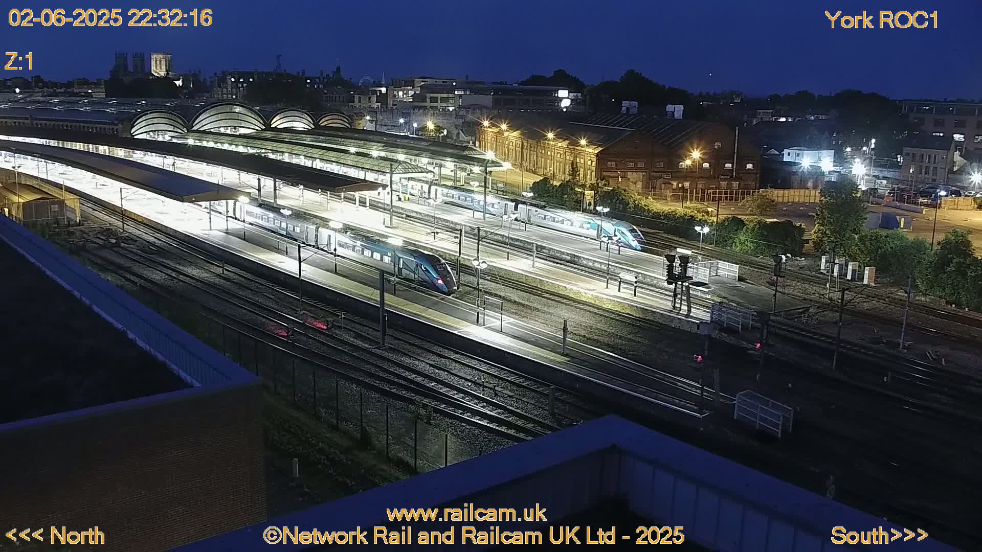 A nighttime, high-angle view of a train station with several lit trains on the tracks.