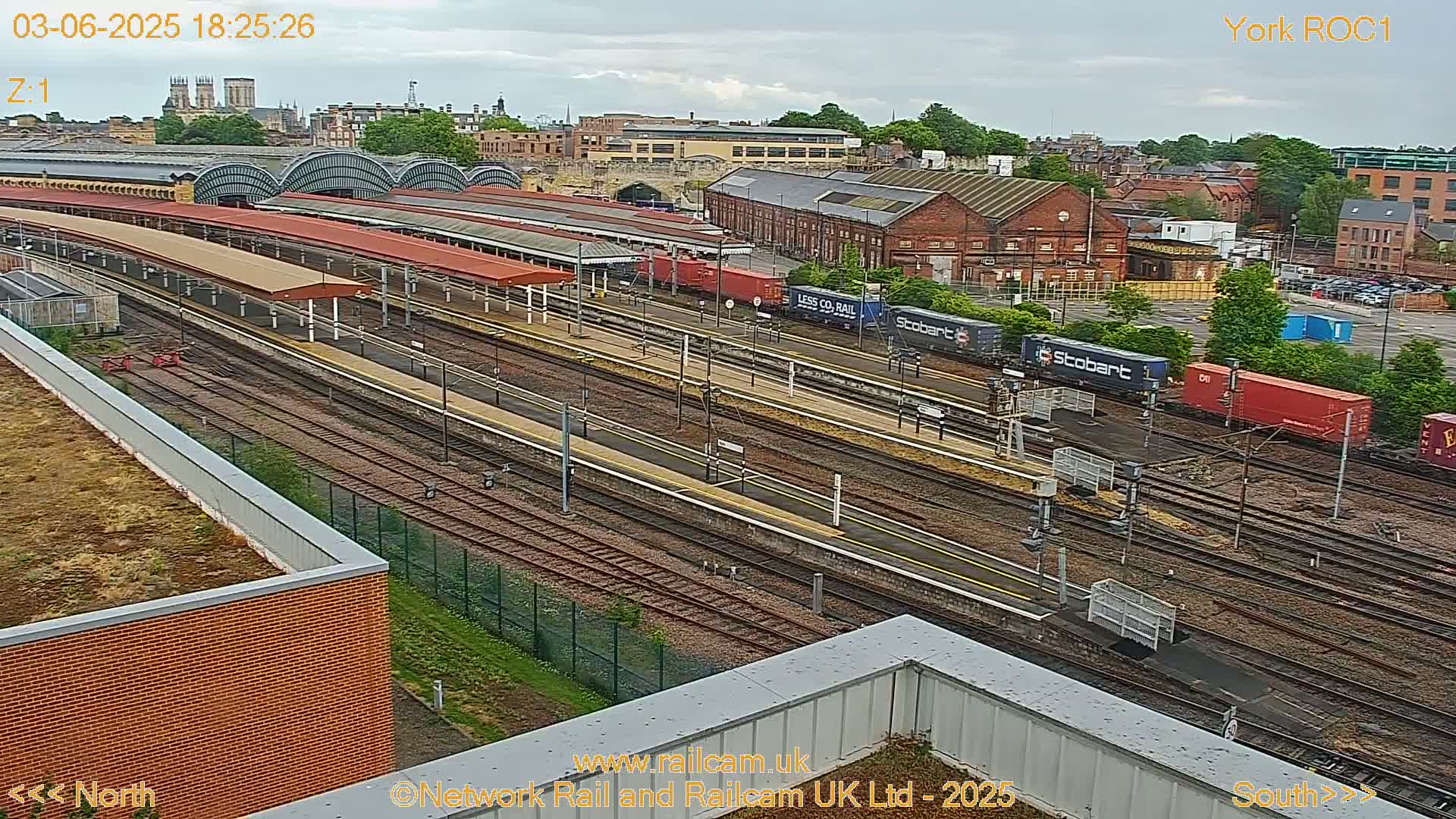 A high-angle view of a train station with multiple tracks and railway cars under an overcast sky.