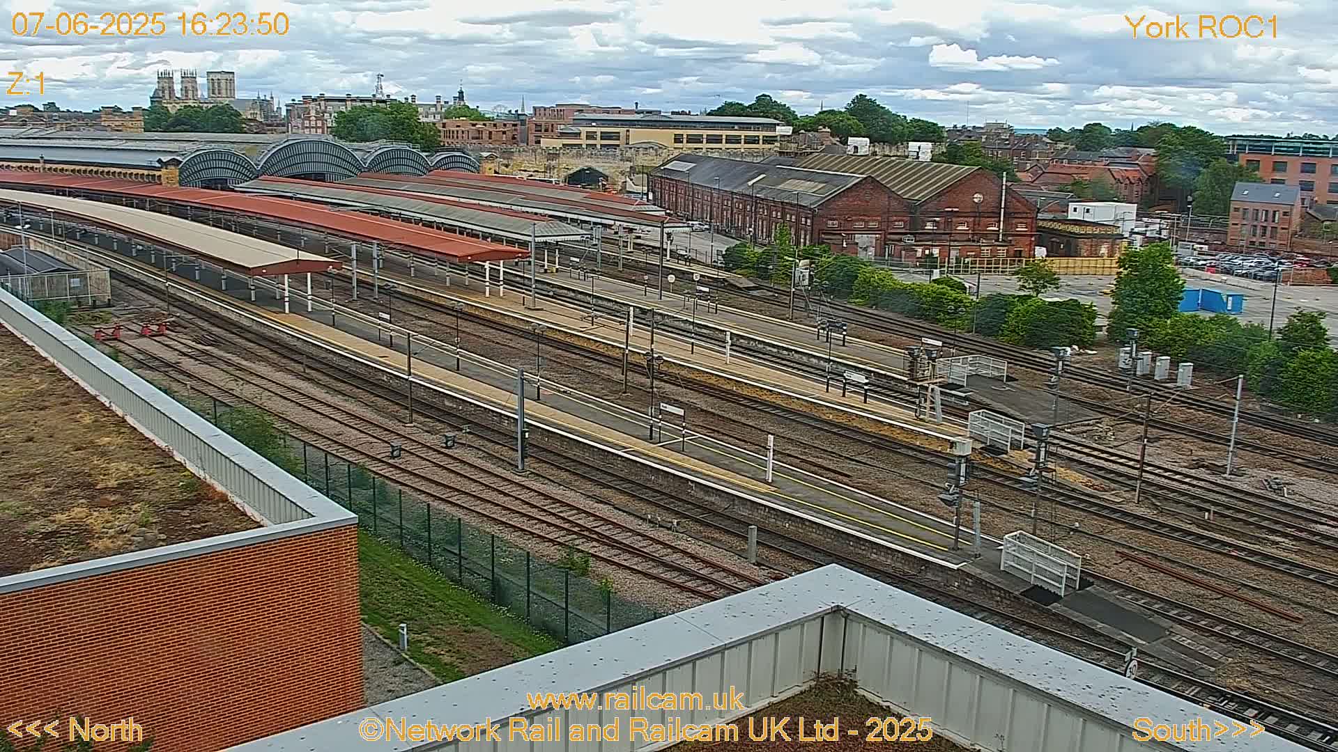 A high-angle view of a train station with many tracks and platforms under a partly cloudy sky.