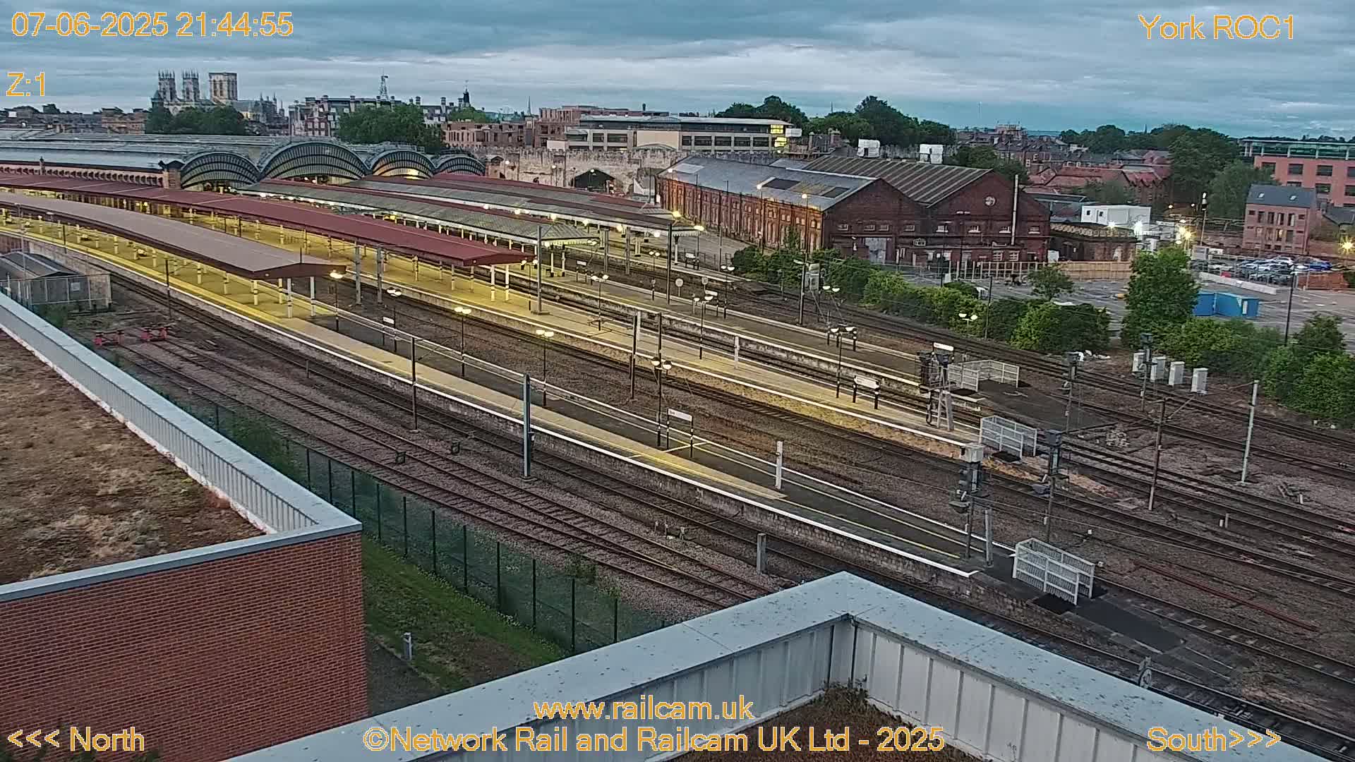 A nighttime aerial view of a train station with many tracks and platforms, under a cloudy sky.