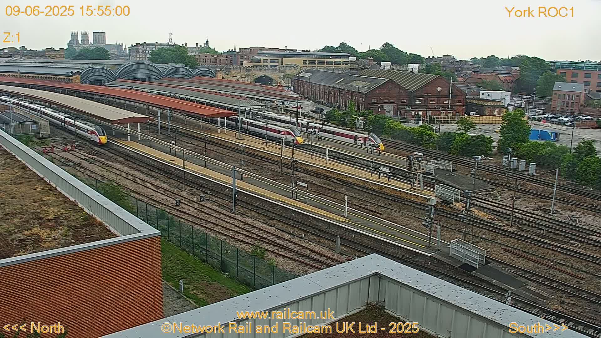 An elevated view of a train station on an overcast day shows several trains at platforms and many railway tracks extending into the distance.