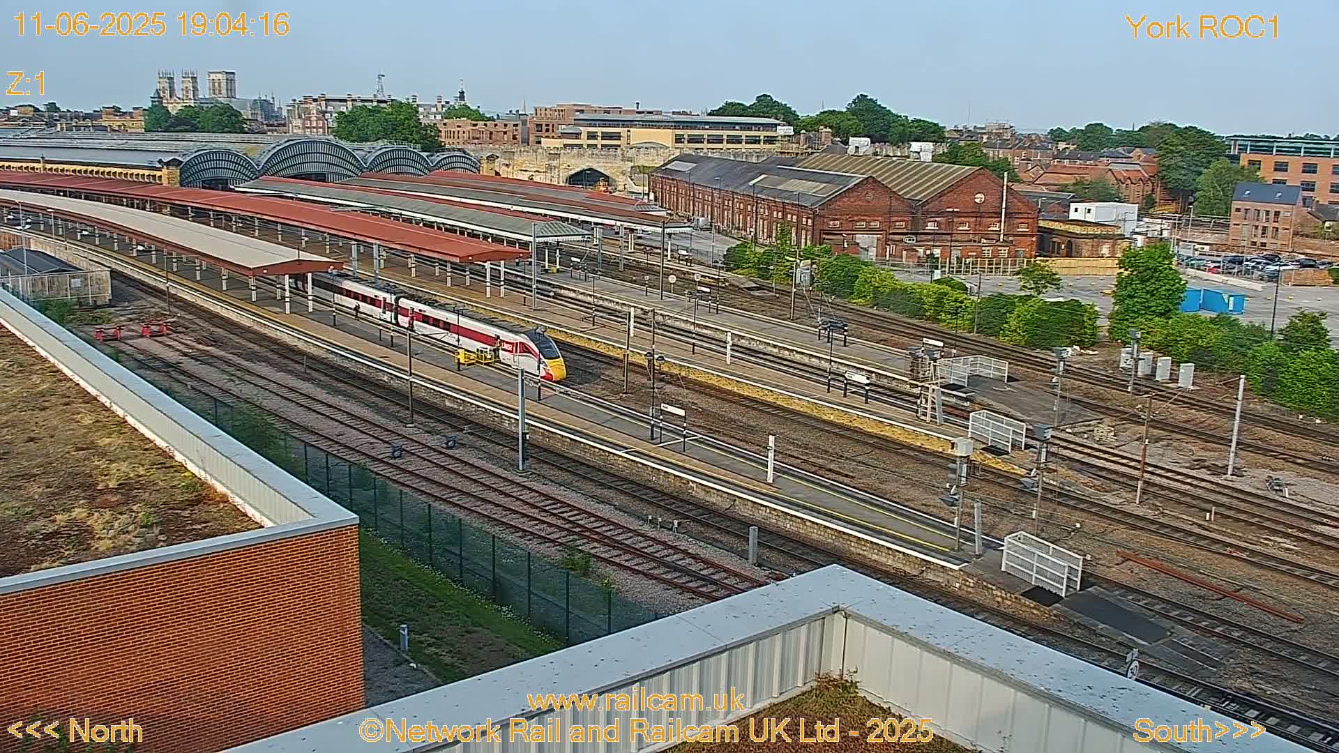 A high-angle view of a train station on a clear day, showing a high-speed train on the tracks and numerous railway lines.