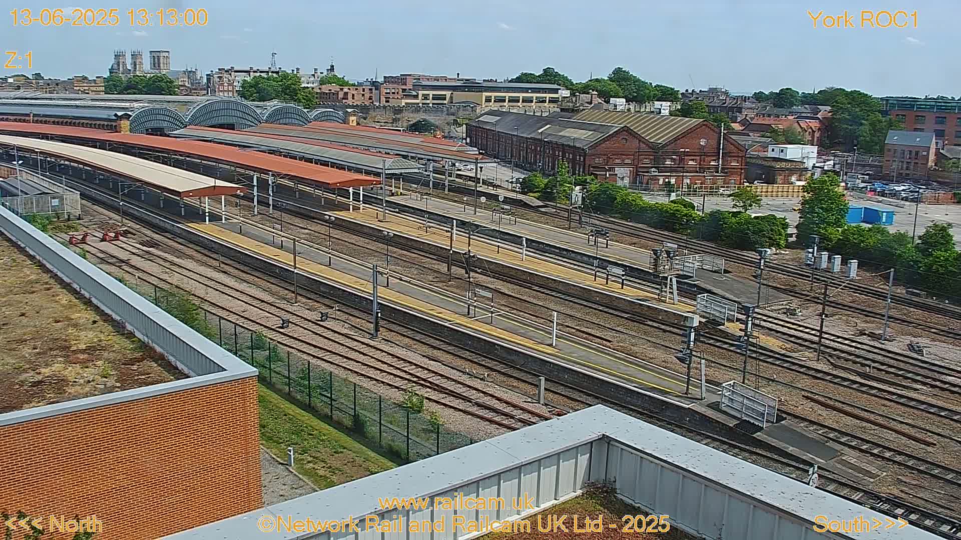 A high-angle view of a train station on a sunny day, showing numerous train tracks and platforms extending into the distance.