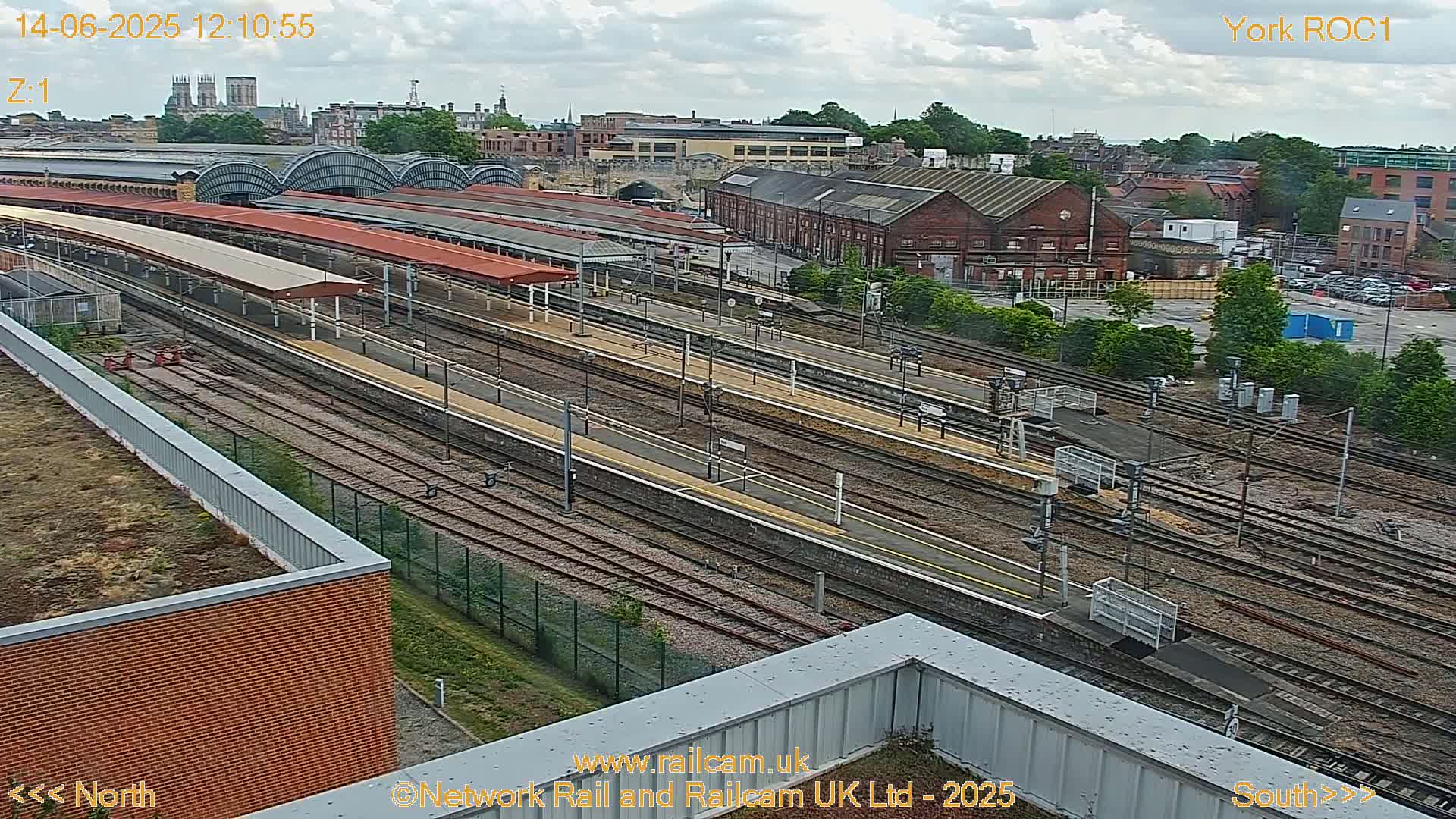 An aerial view of a railway station and its surrounding area on a partly cloudy day.