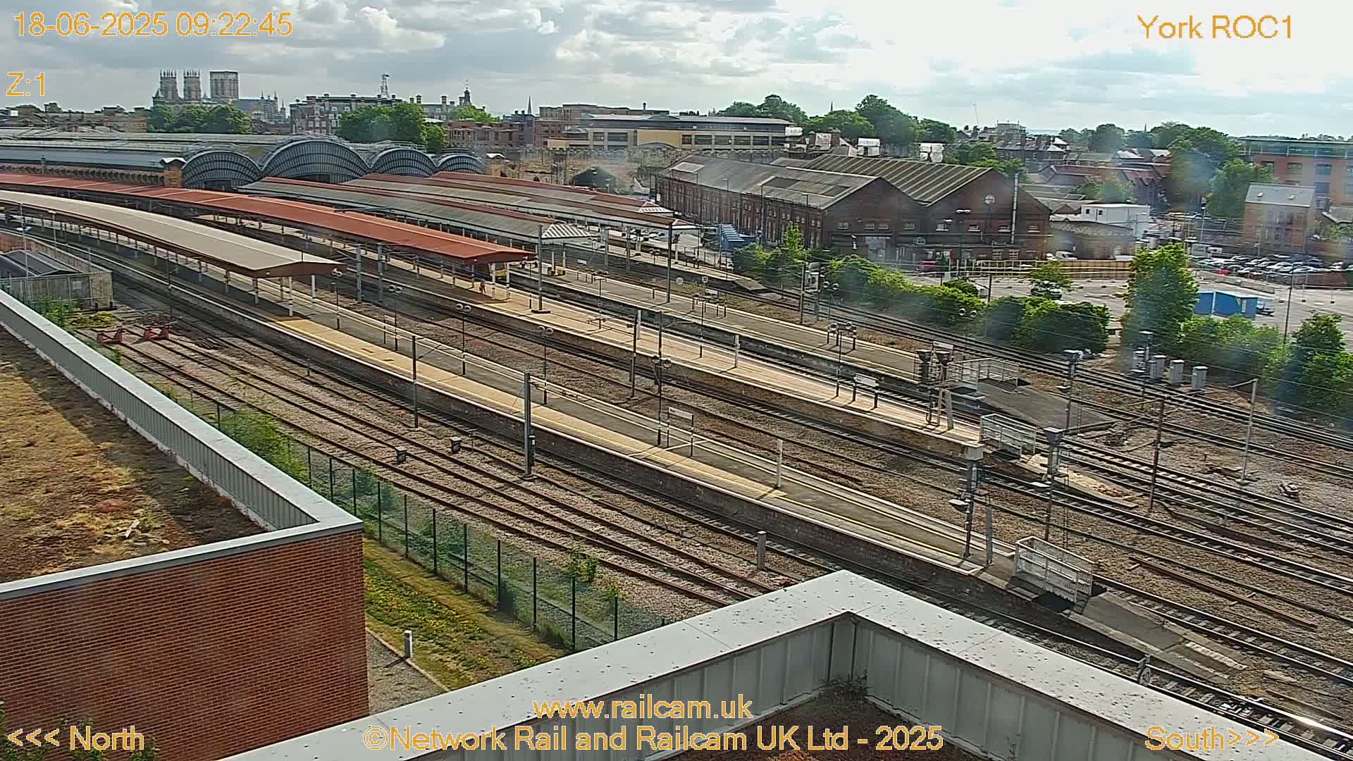 A high-angle view of a train station with numerous tracks and platforms under a partly cloudy sky.