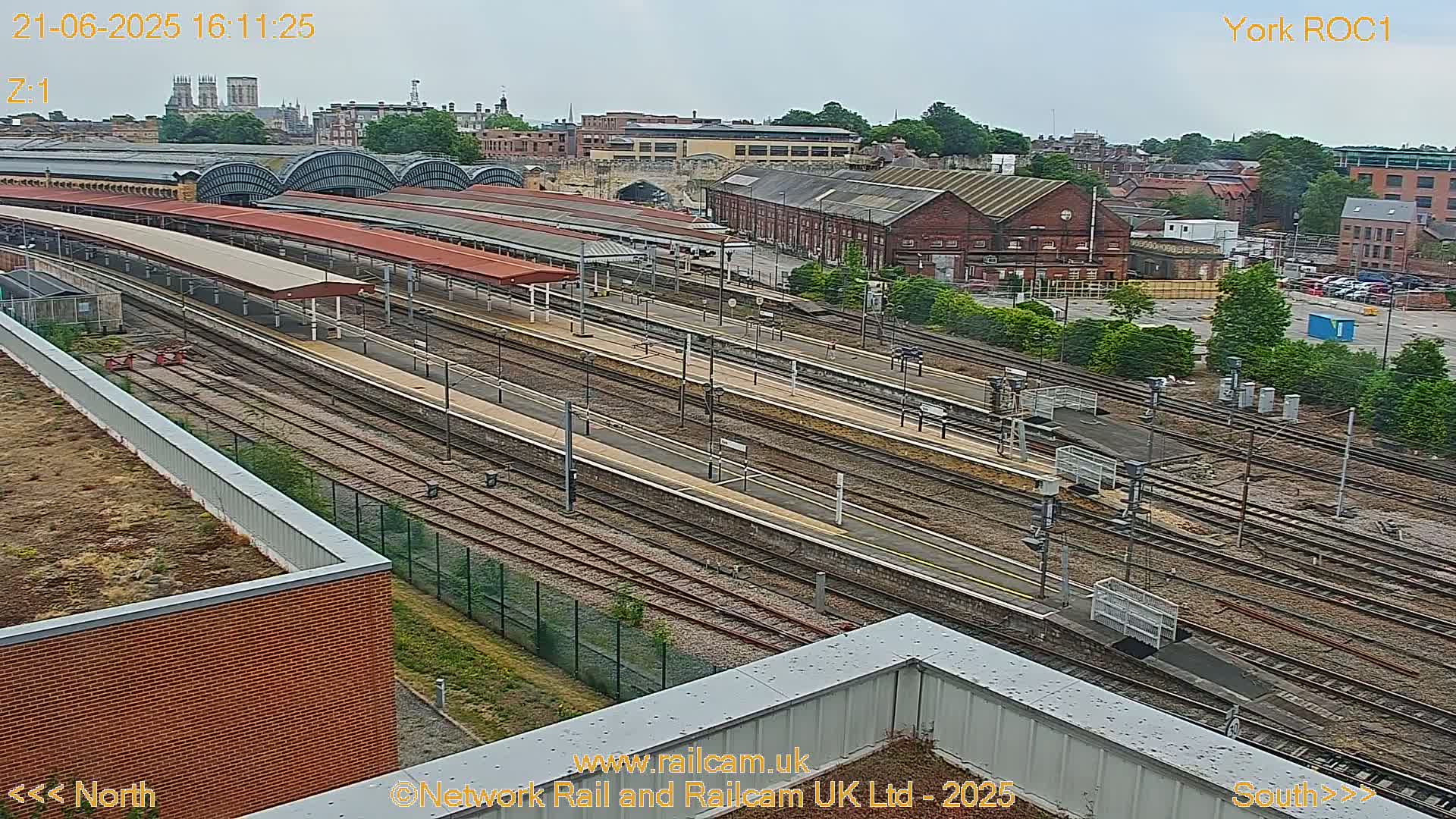 A high-angle view of a train station with numerous tracks and platforms on an overcast day.