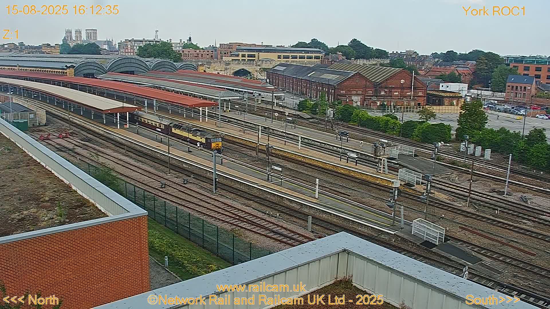 A long, dark train moves through a brightly lit train station at night.