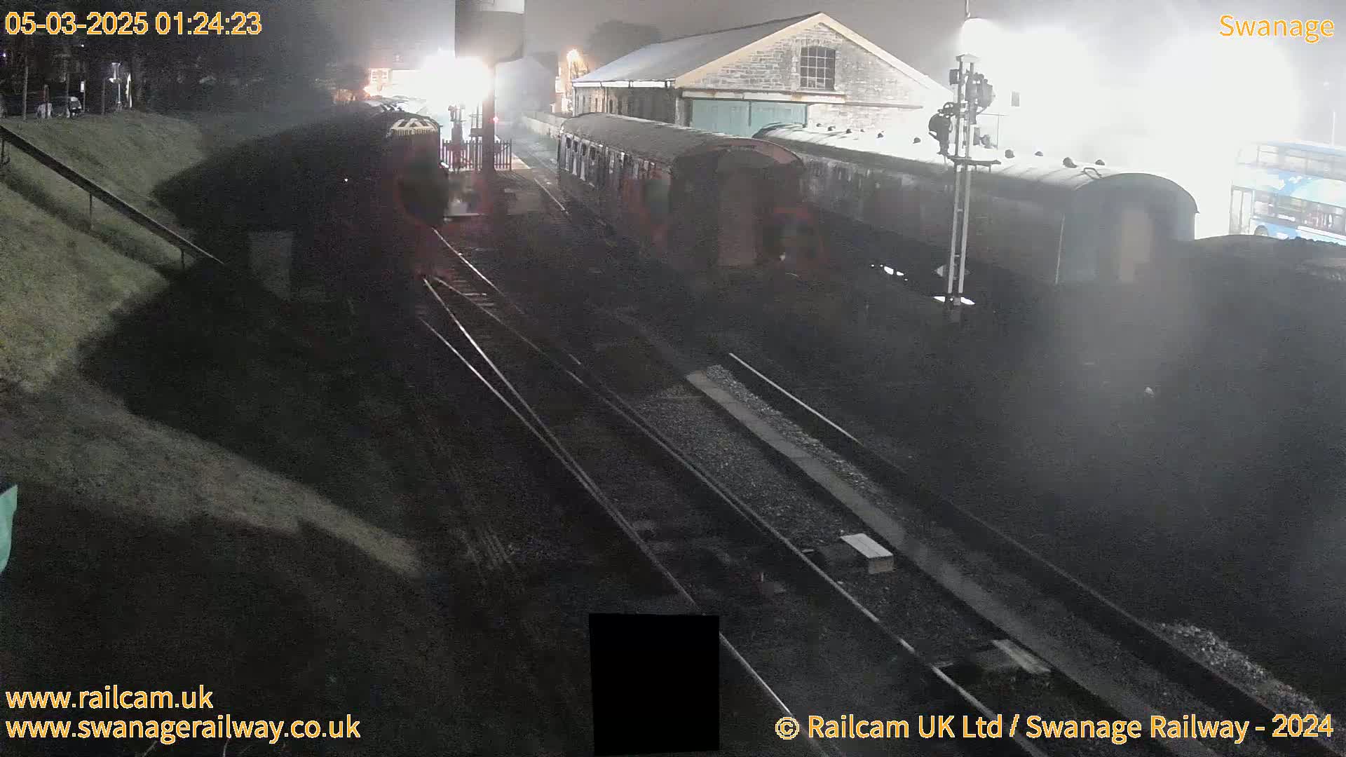 A nighttime view of a train at a station on multiple tracks, with misty or foggy conditions.
