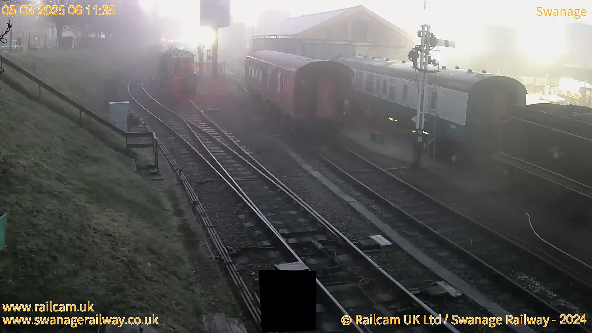 Several train cars and a locomotive are parked on railway tracks in foggy conditions.