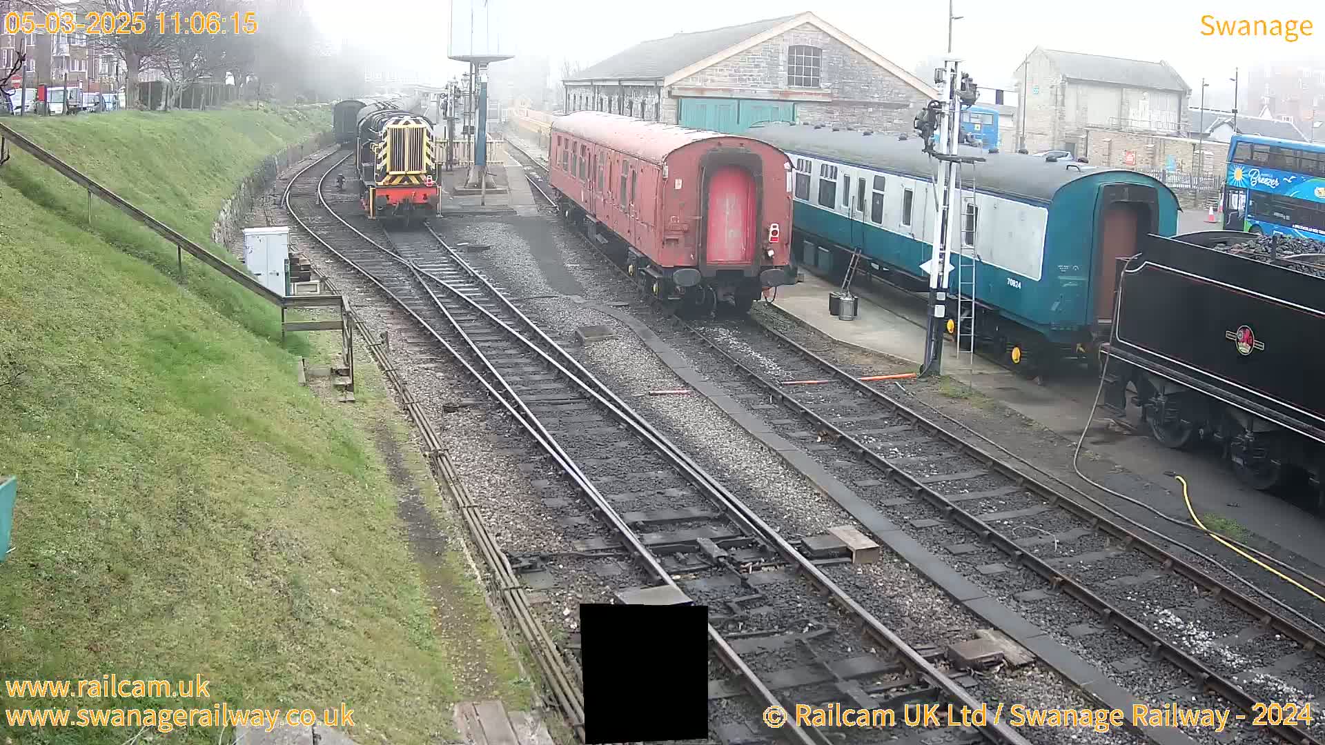 A foggy view of several train cars and locomotives parked on railway tracks next to a stone building.