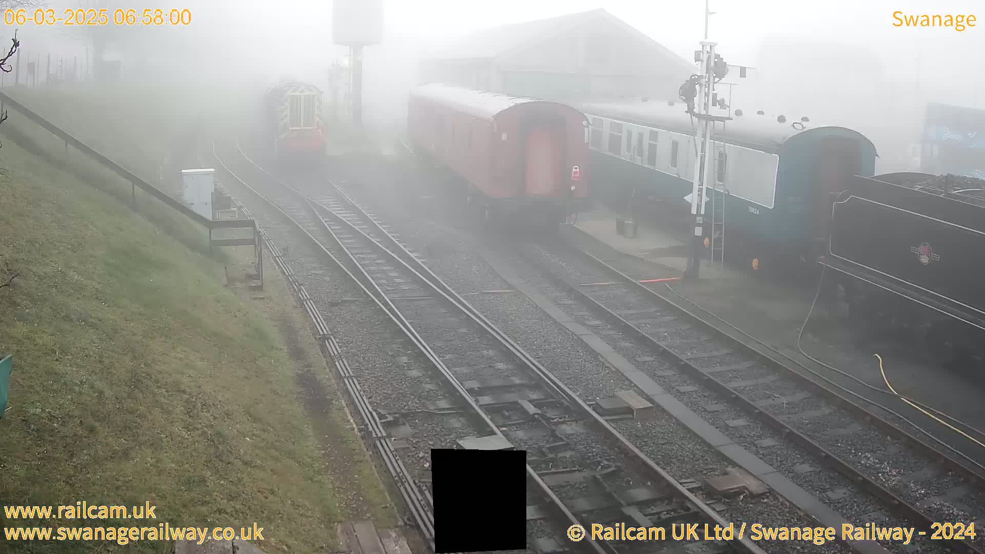 Several train cars and a locomotive are visible on railway tracks in thick fog.