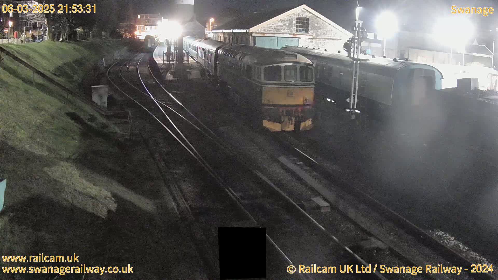 A diesel train sits at a nighttime train station next to several other train cars.