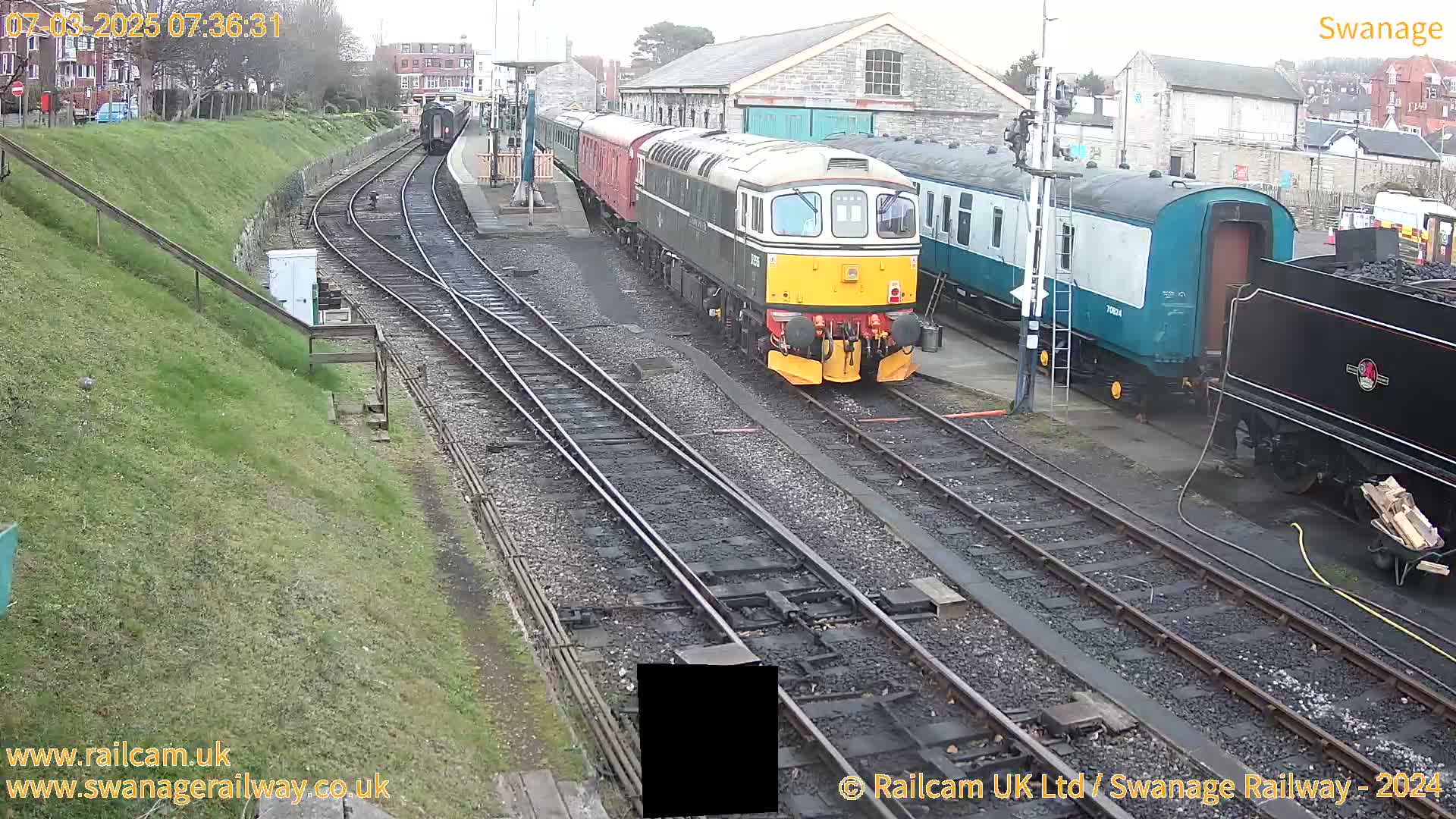 A train station with multiple train cars and locomotives on several tracks, on an overcast day.