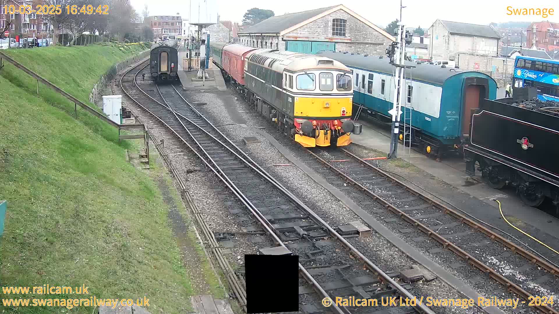 Several train cars and locomotives are parked on railway tracks next to a stone building on an overcast day.