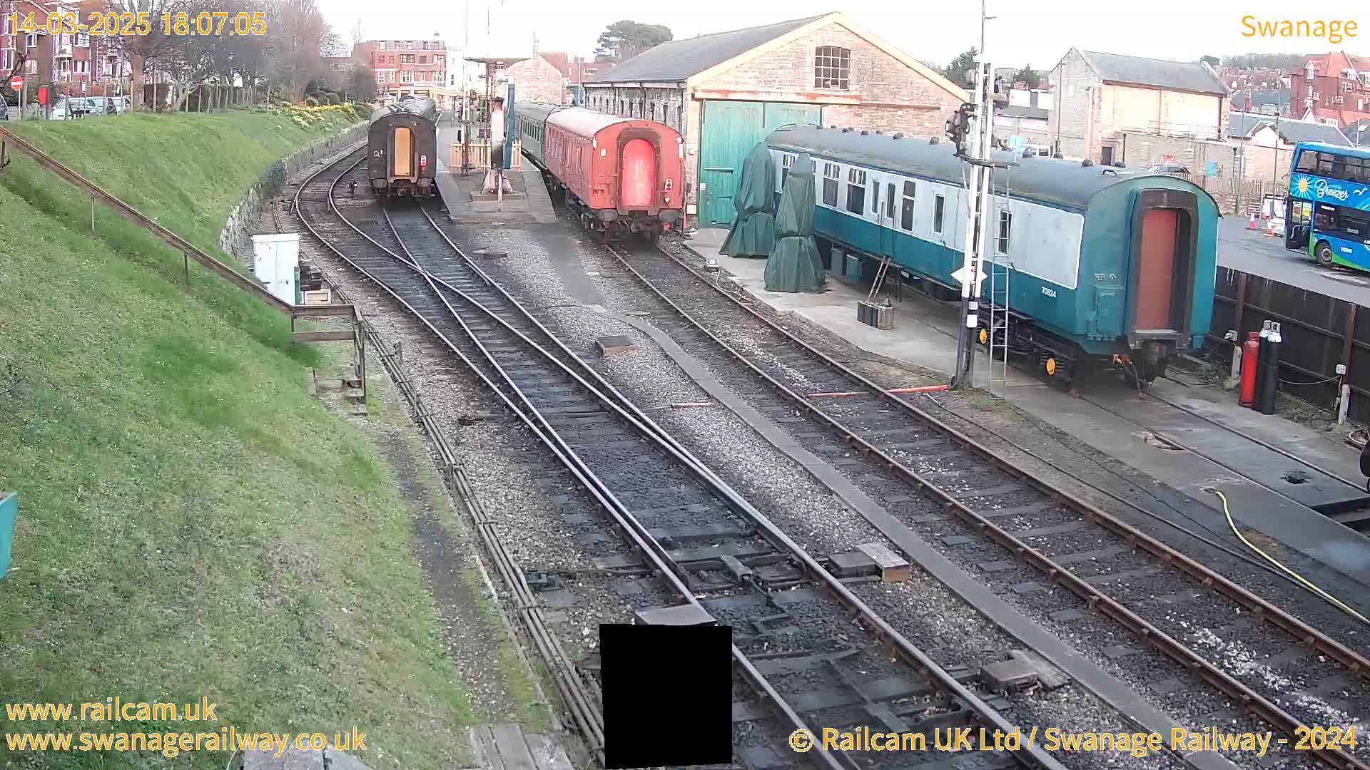 Several railway carriages are parked on tracks near a railway building on an overcast day.