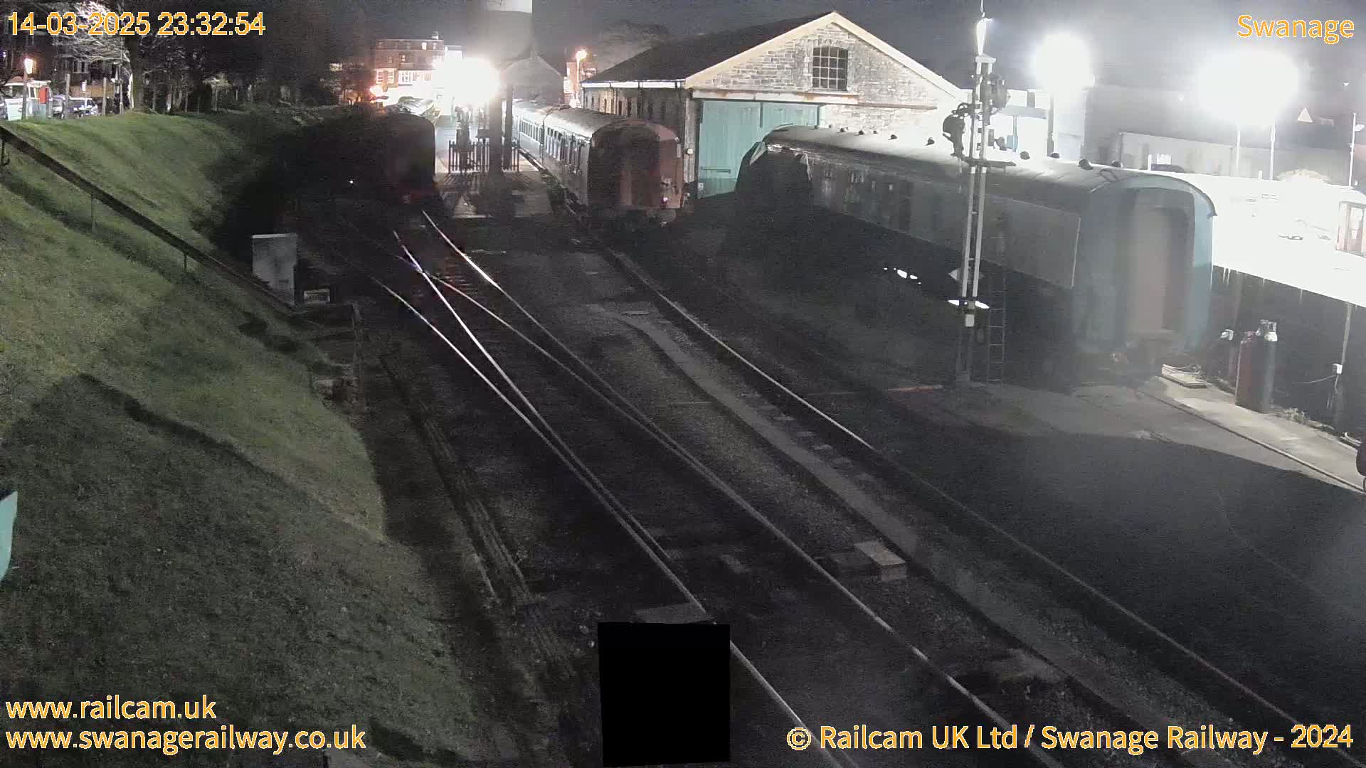 At night, several railway cars are parked near a building beside train tracks.