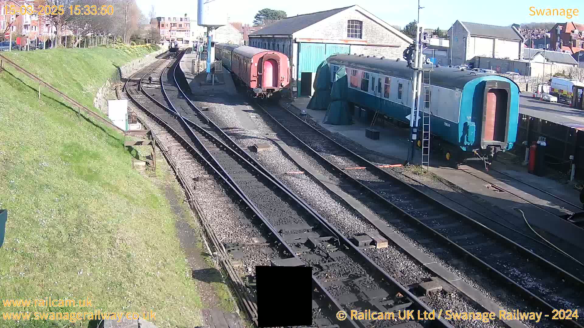 Several railway carriages are parked on railway tracks next to a stone building on a sunny day.