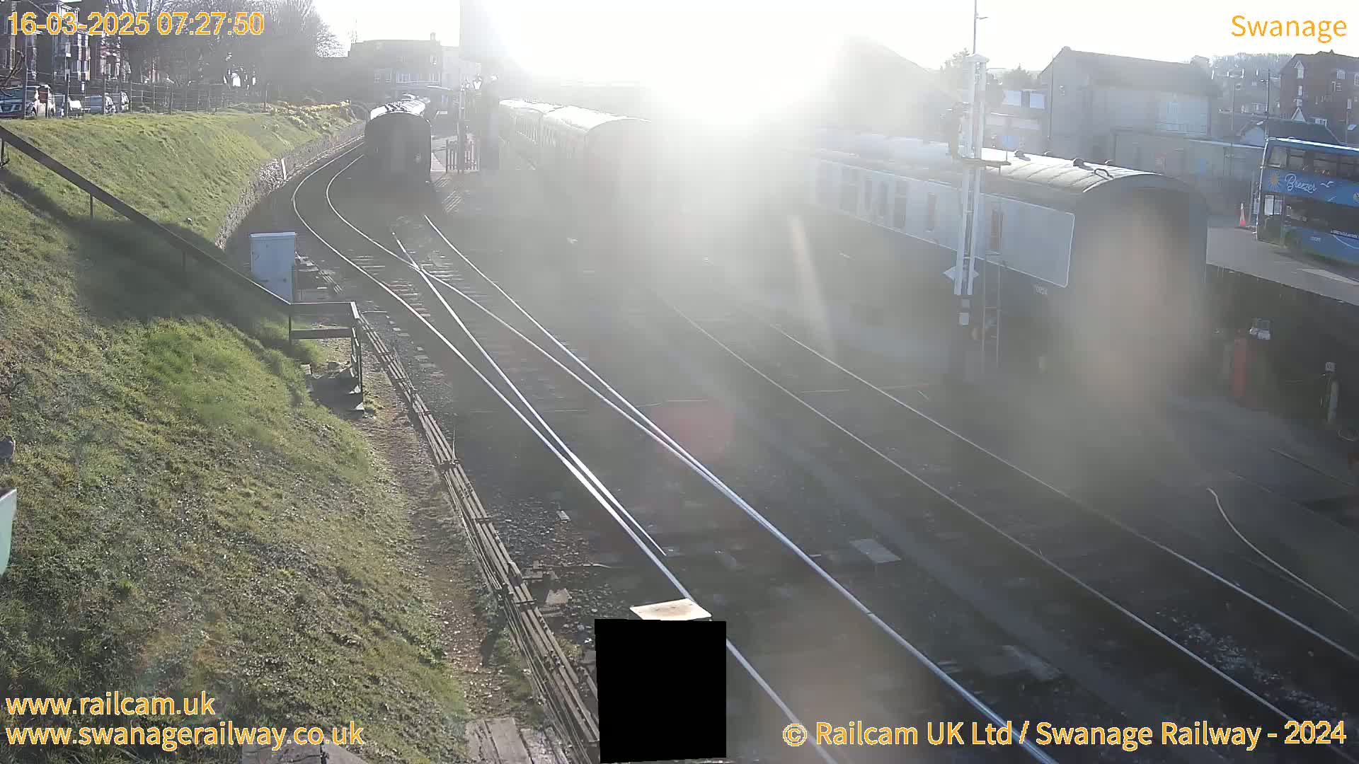 A train sits in a brightly lit train station on a sunny day.