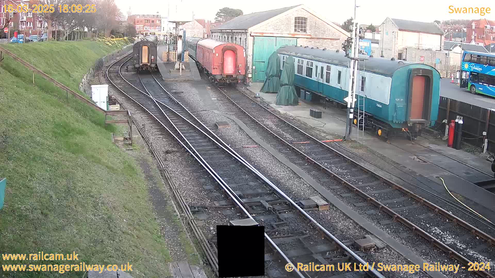 Several railway cars are parked on tracks next to a railway station building under a cloudy sky.