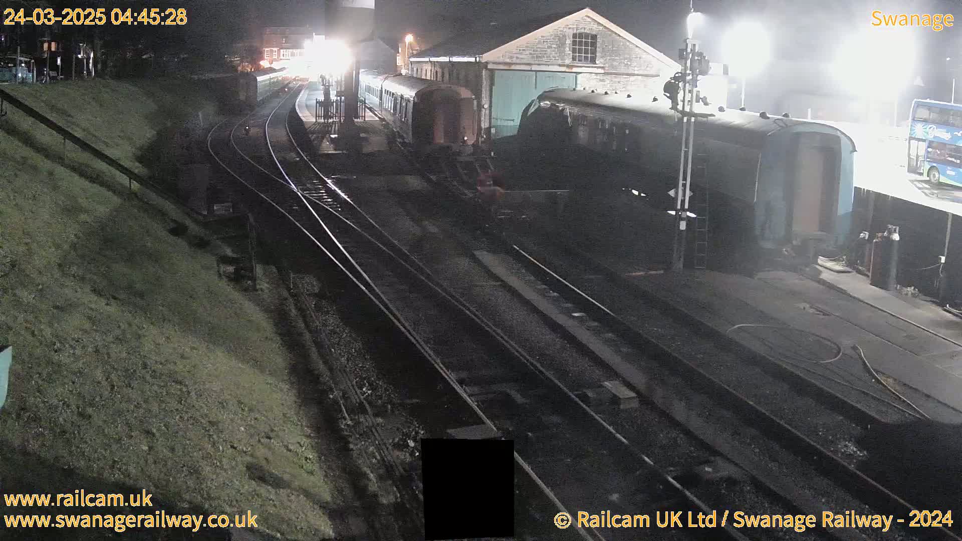 At night, several train cars are parked at a station next to a building, under bright lights.