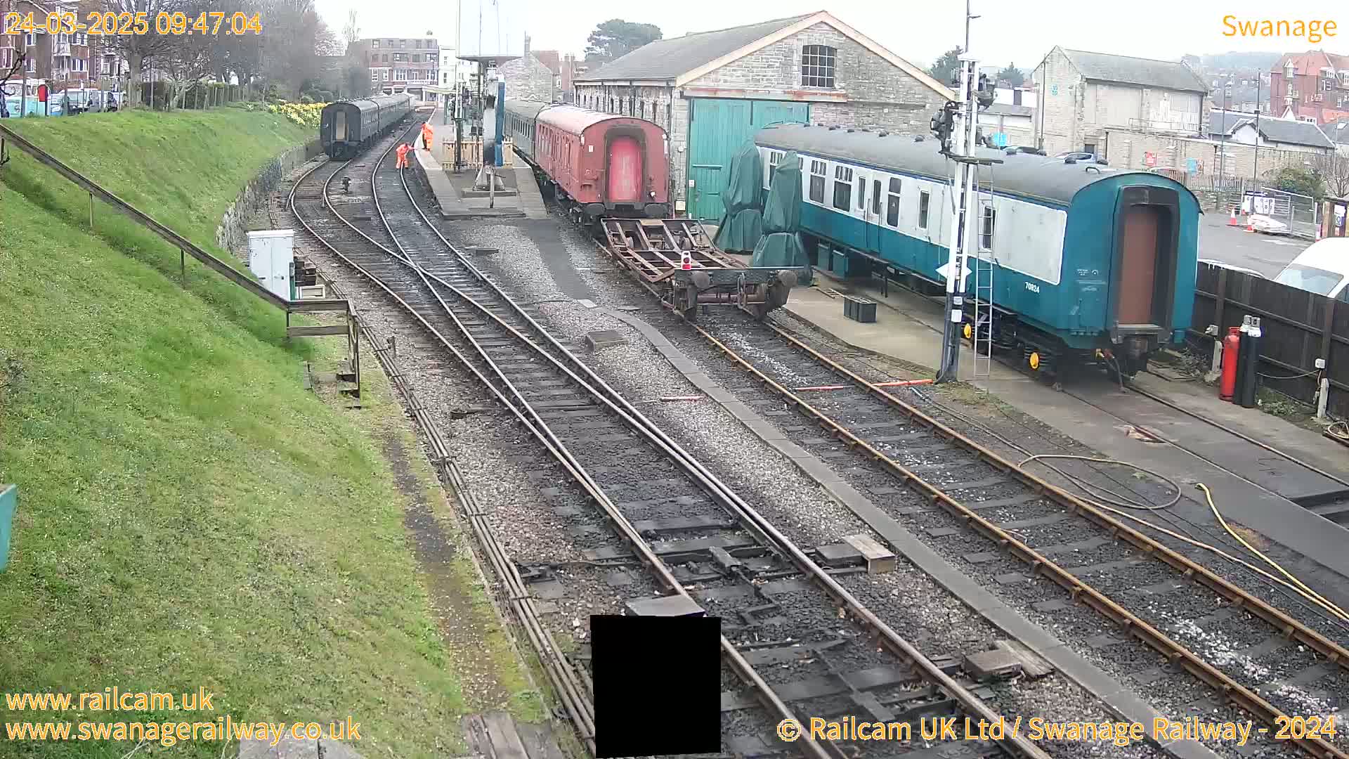 Several railway carriages are parked on train tracks next to a railway station building on an overcast day.
