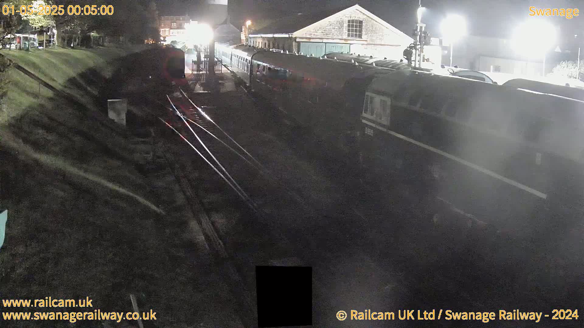 A long dark train sits at night in a railway station next to a building.
