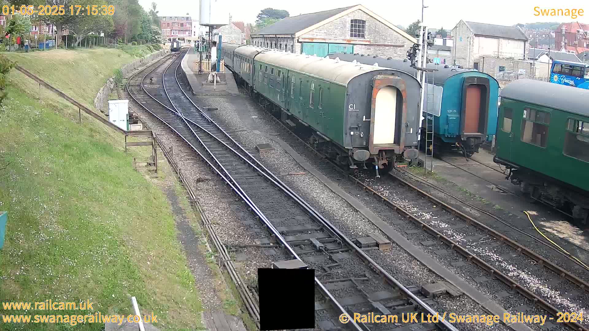 Several railway carriages are parked on train tracks in a station yard on an overcast day.
