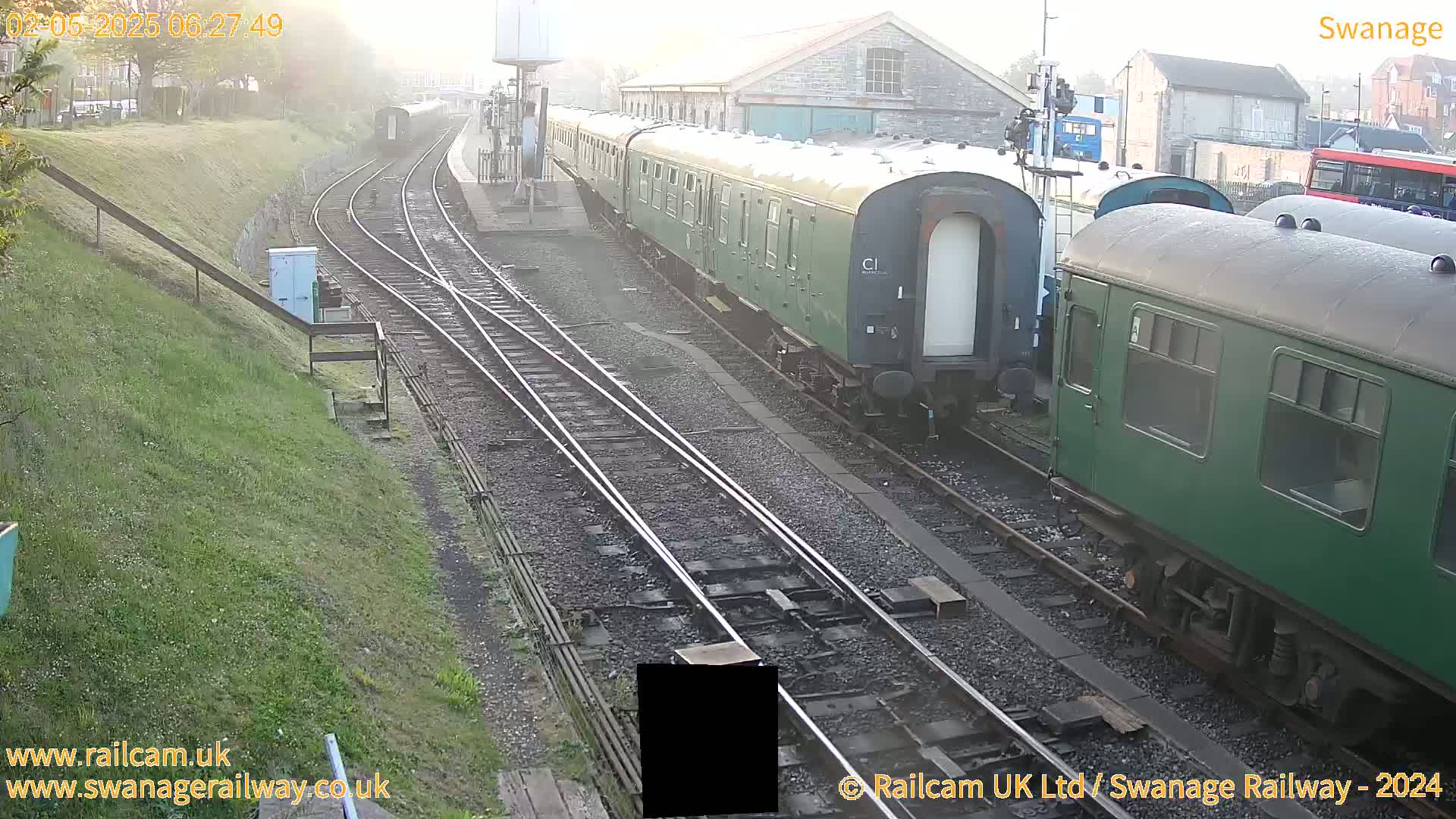 A misty morning at a train station shows several green passenger train cars on railway tracks.