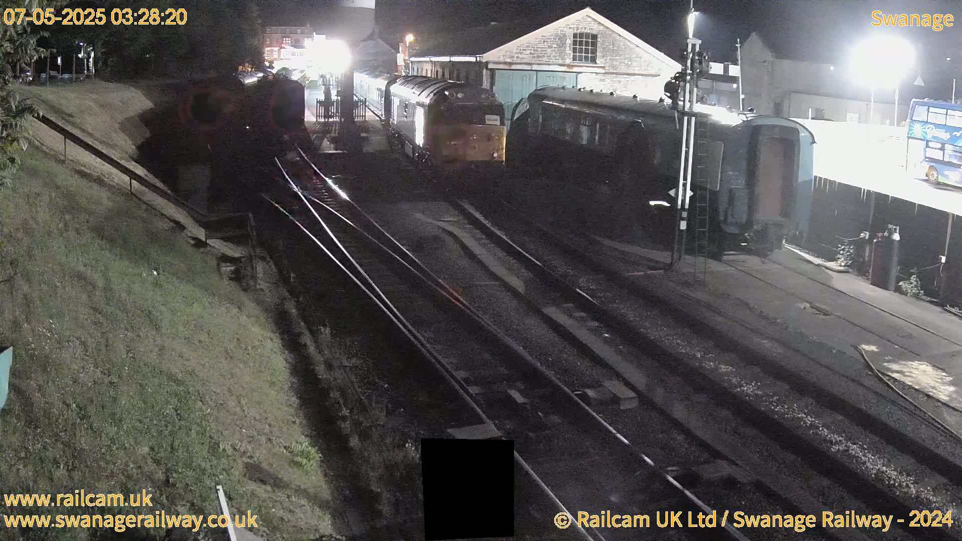 At night, a train sits on railway tracks next to a building, partially obscured by darkness.