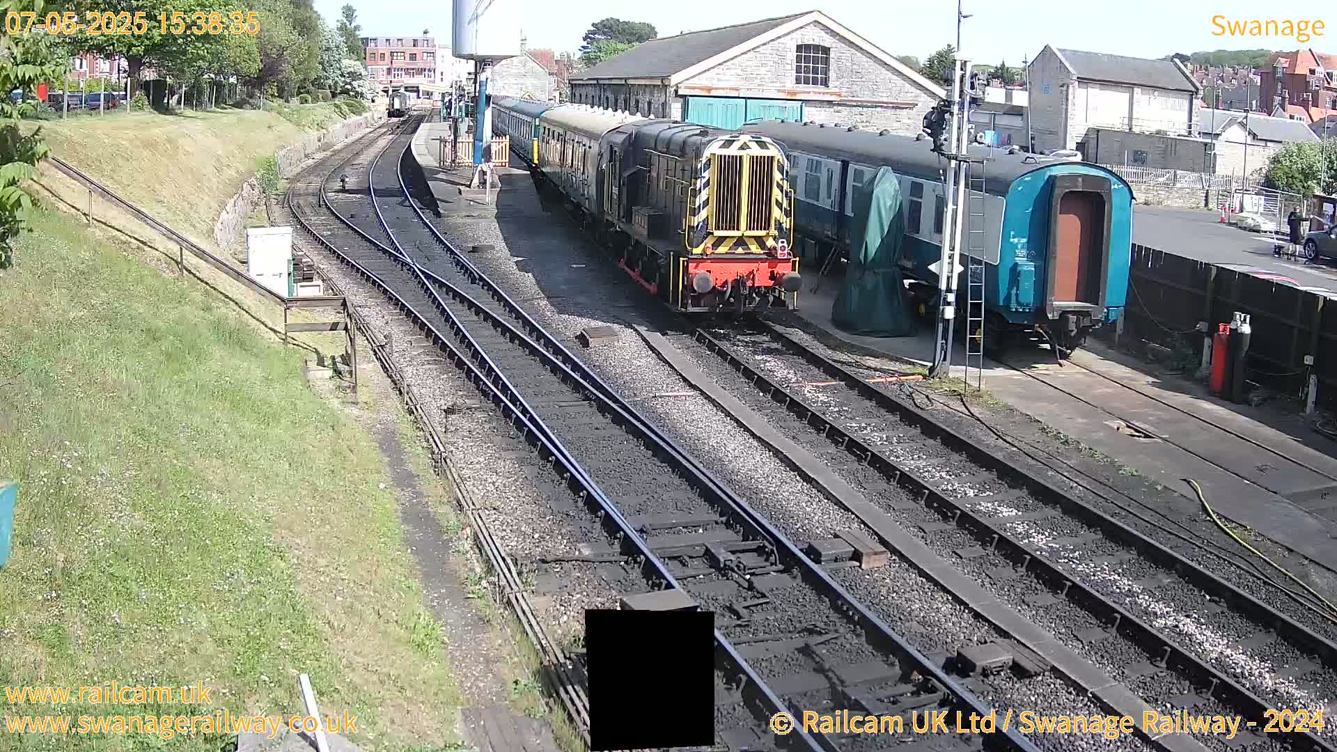 A diesel locomotive pulls a train of passenger cars along railway tracks on a sunny day.