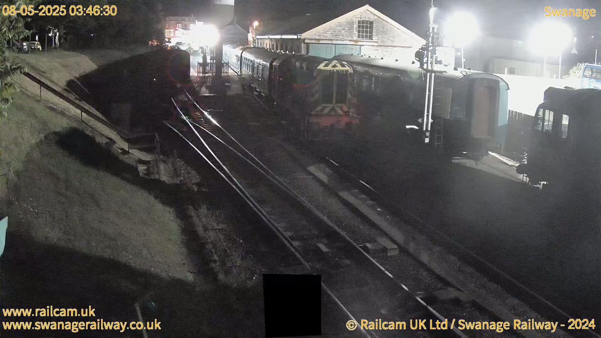 At night, a train sits at a station on train tracks next to a building.