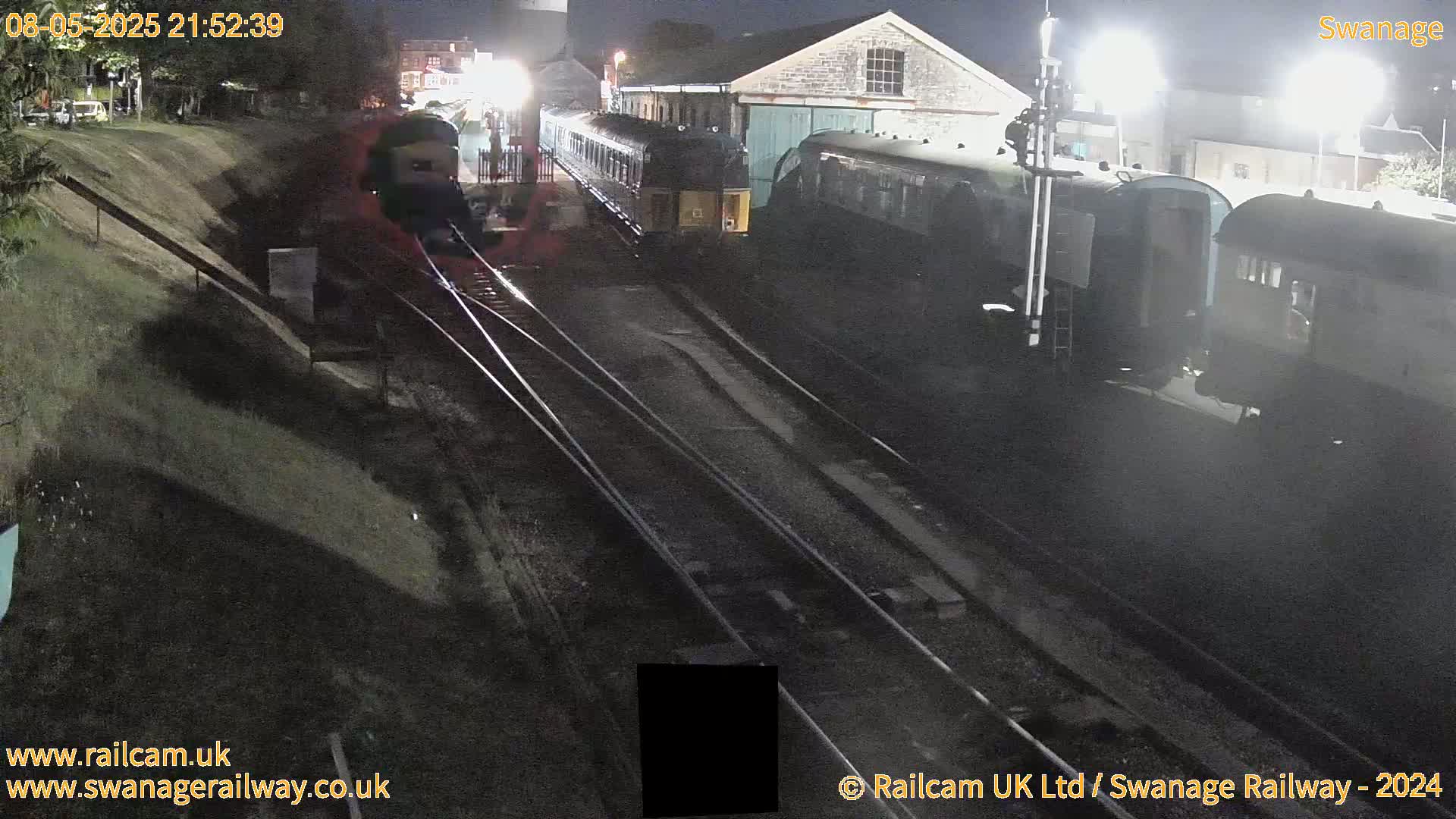 At night, several railway cars are parked near a building alongside train tracks.