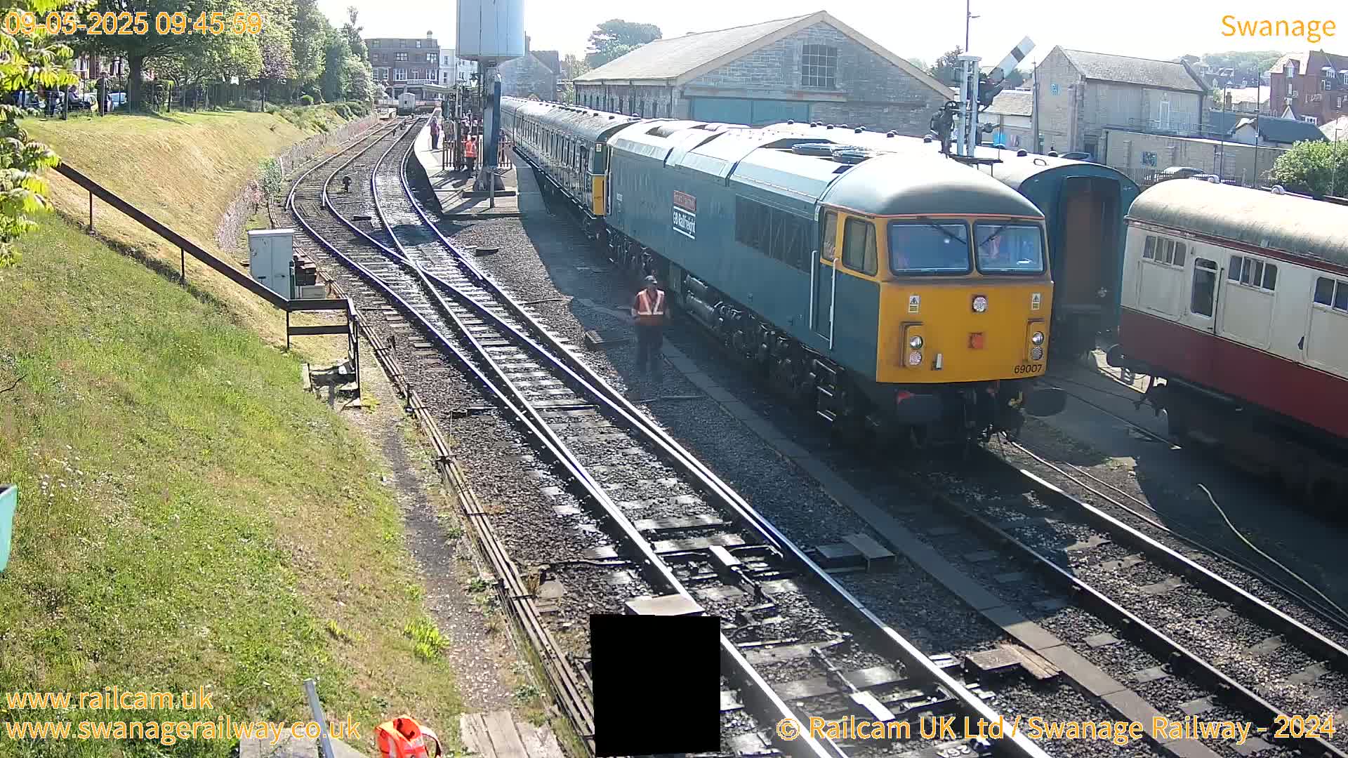A blue and yellow diesel locomotive pulls a train of passenger cars along train tracks on a sunny day.