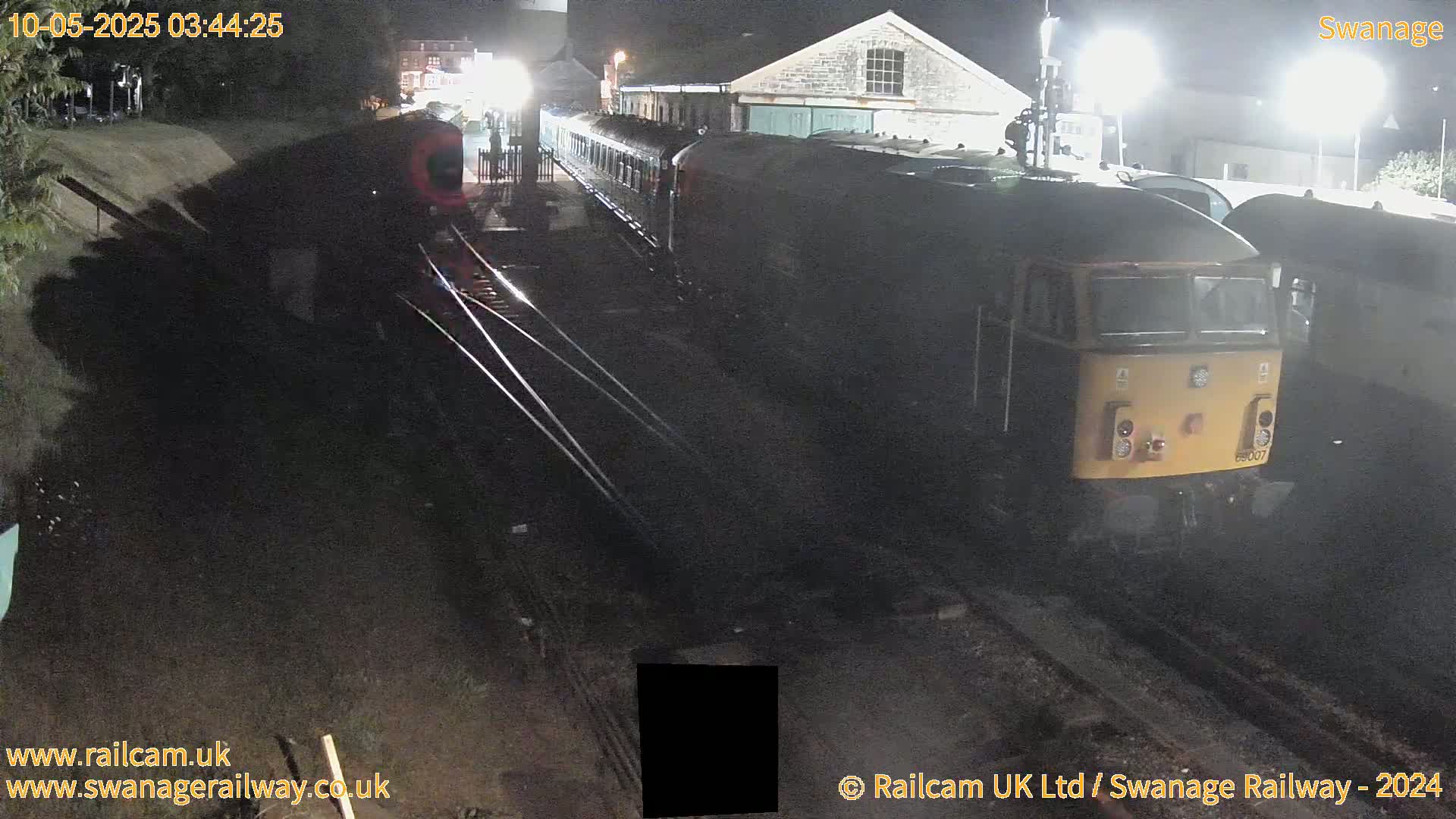 At night, a diesel locomotive and train cars sit on railroad tracks next to a building.