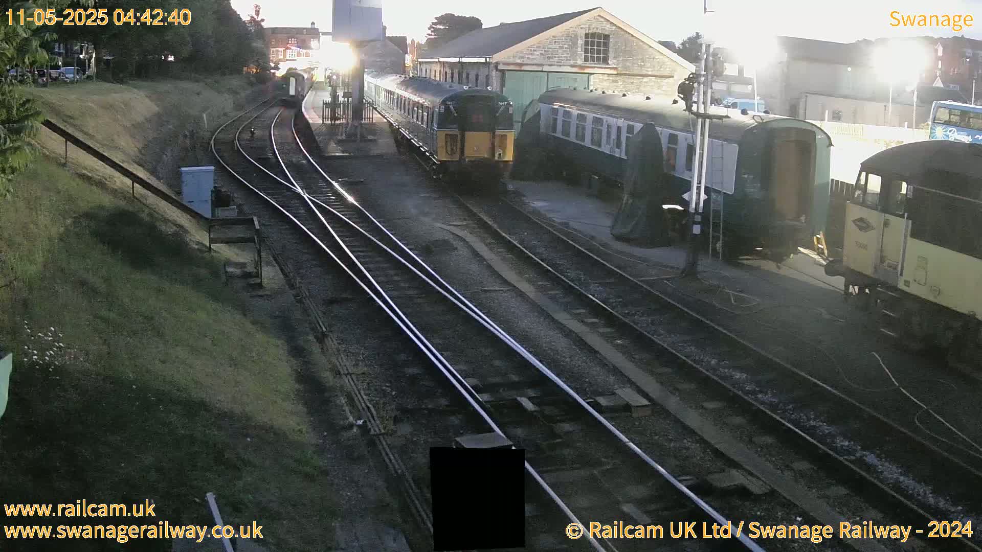 Several railway carriages and a train are parked at a station under twilight conditions.