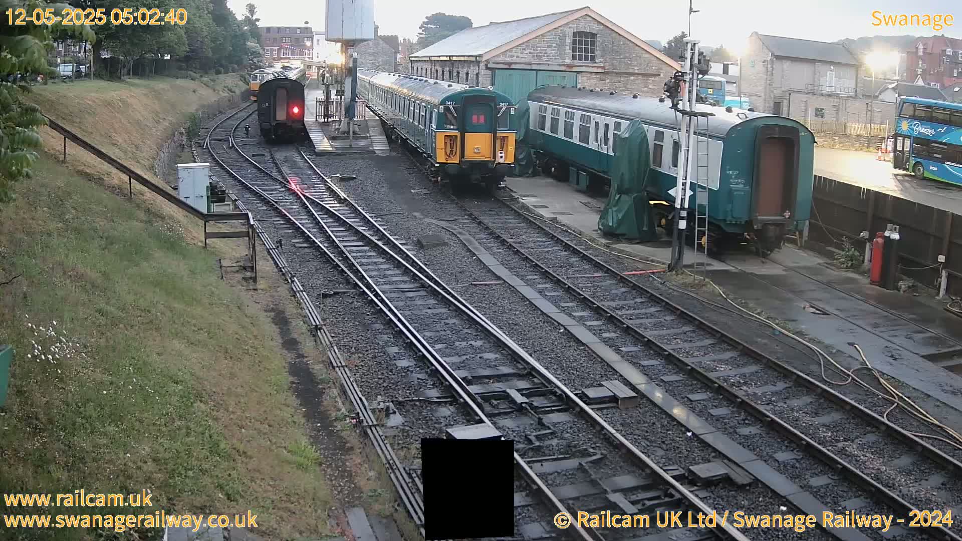 Several railway carriages and a train are parked on railway tracks next to a stone building in the early morning.