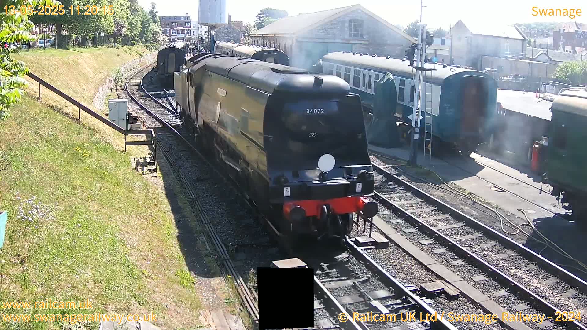 A black diesel locomotive leads a train of passenger cars along railway tracks on a sunny day.