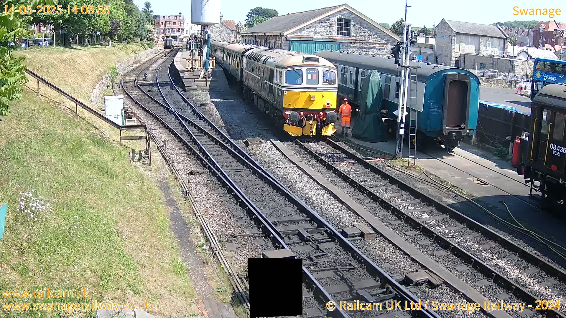A yellow and green diesel train is parked on railway tracks next to several other train cars on a sunny day.