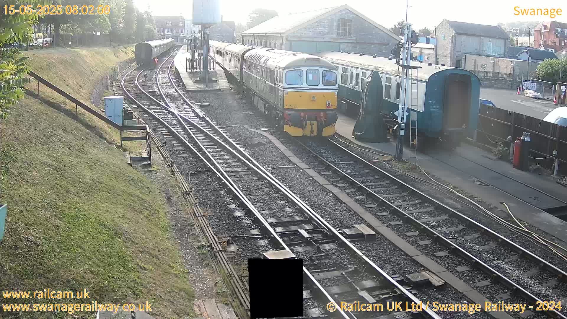 A diesel train is stopped at a railway station on a partly sunny day.