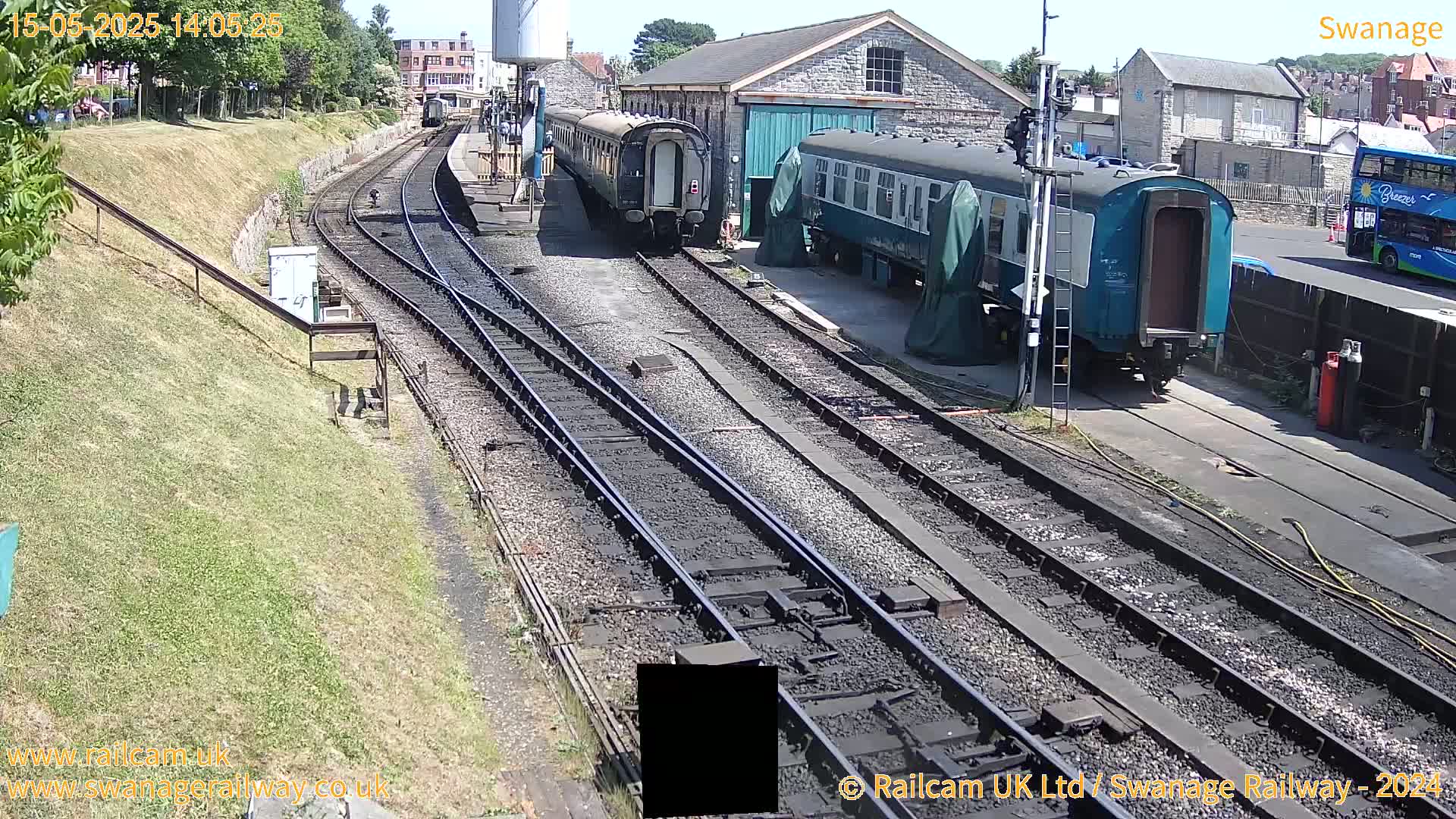 Several railway cars are parked on train tracks next to a stone building on a sunny day.