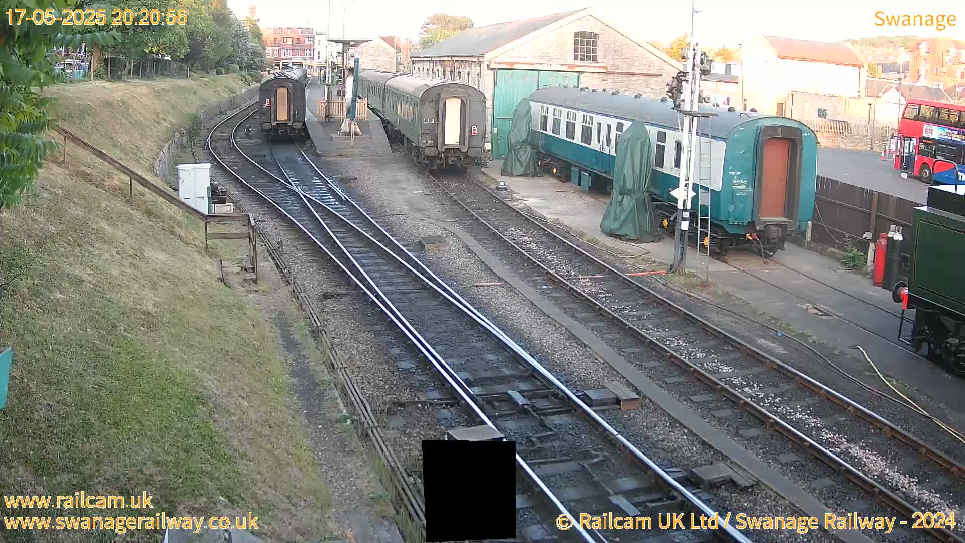 Several railway carriages are parked on multiple train tracks next to a railway station building on a partly cloudy day.