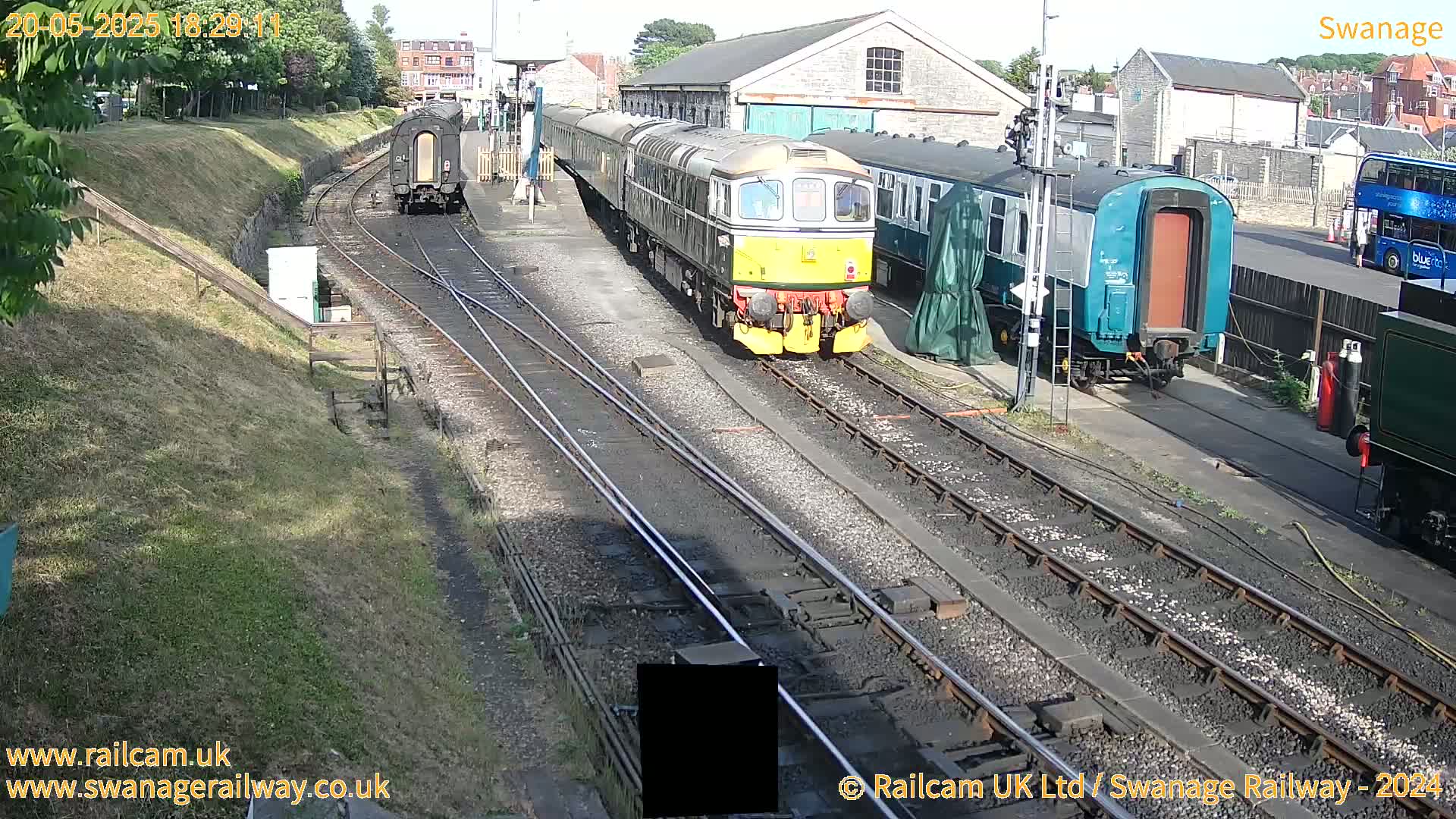 A passenger train is stopped at a railway station on a sunny day.